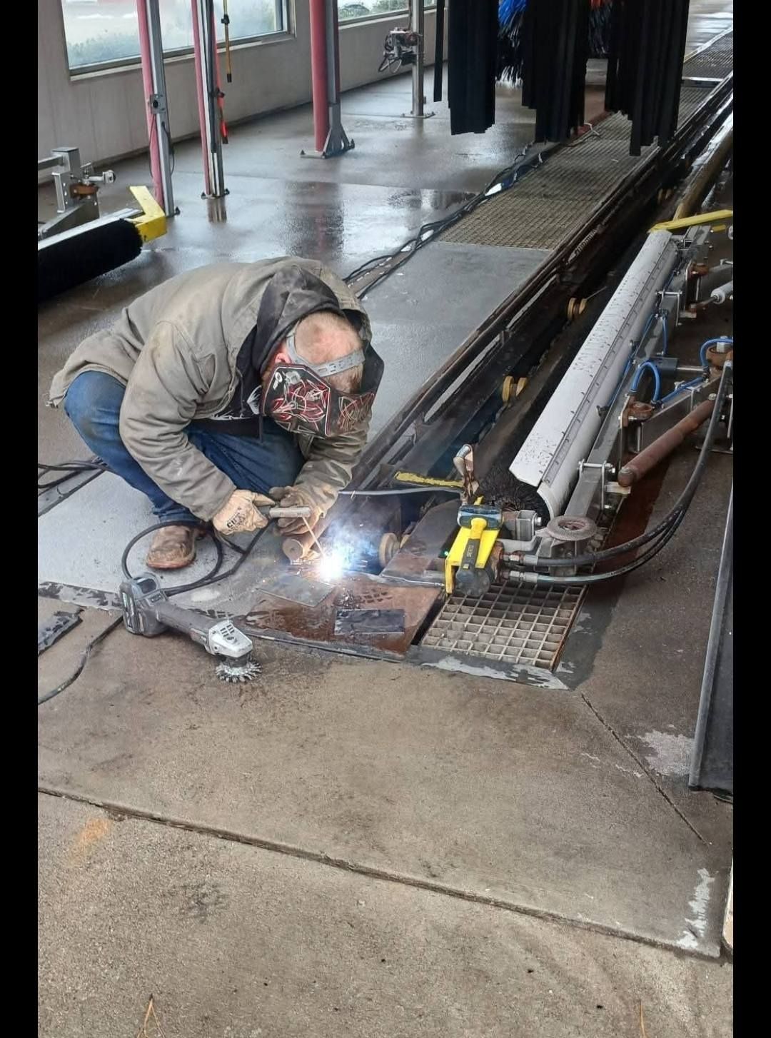 Person welding metal in a car wash bay. Sparks fly as they work on a metal grate, with a grinder nearby.