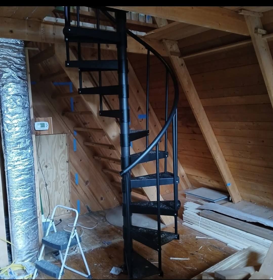 Black spiral staircase in an attic with wood walls, step stool, and insulation.