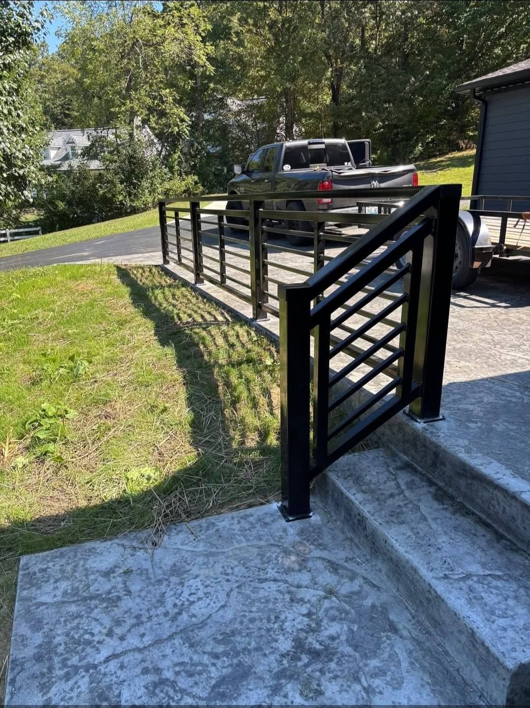 Black metal railing on concrete steps and path, green lawn, truck in background.