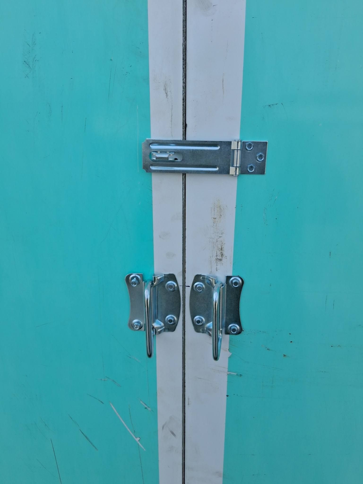 Teal metal doors with white trim, secured by a silver latch and two silver hasp sets.