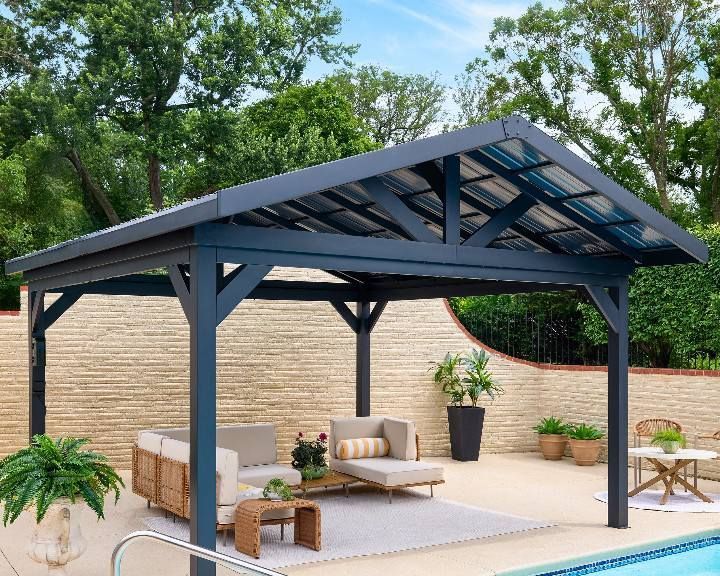 Outdoor gazebo with dark gray frame and see-through roof over patio furniture by a pool.