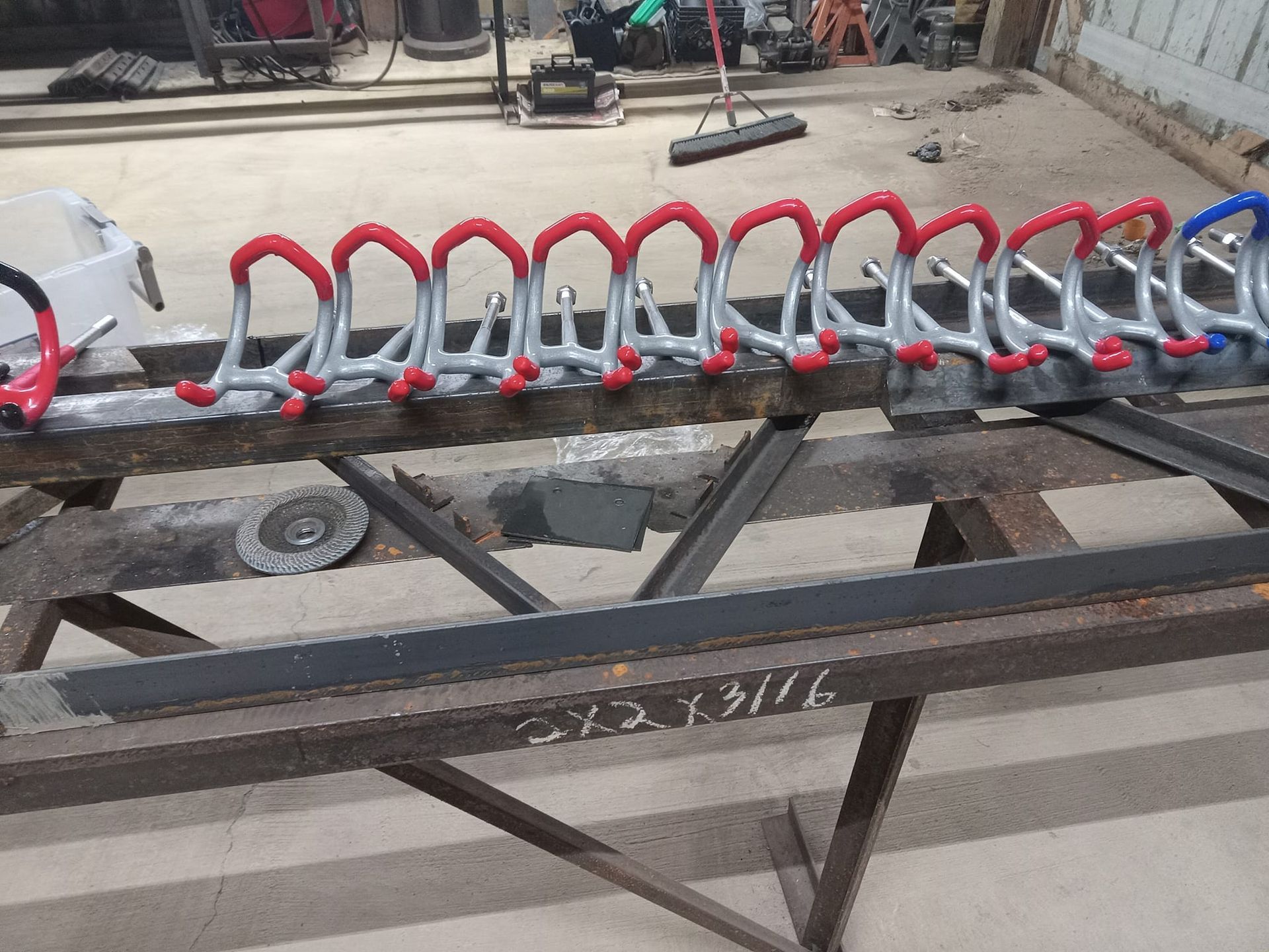 Metal bike rack with red and blue rubber coated supports, sitting on a welding table.