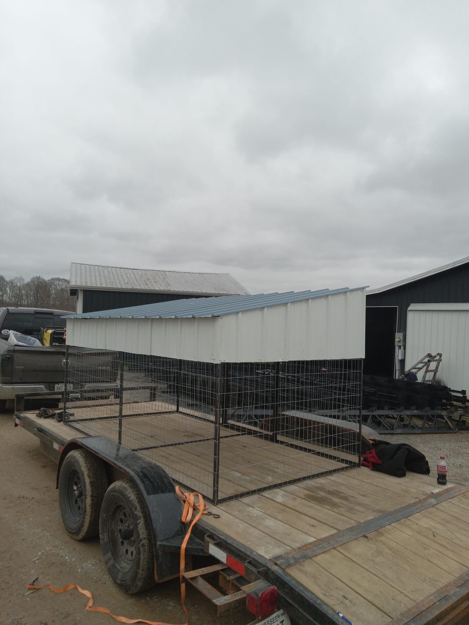 Metal structure on trailer, white and blue roof, outdoors, overcast sky.