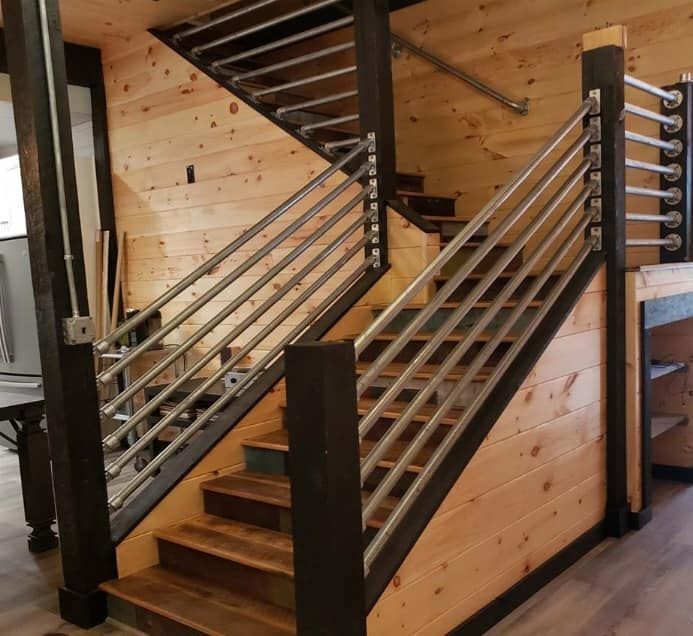 Wooden staircase with horizontal metal handrails and dark posts, inside a wood-paneled room.