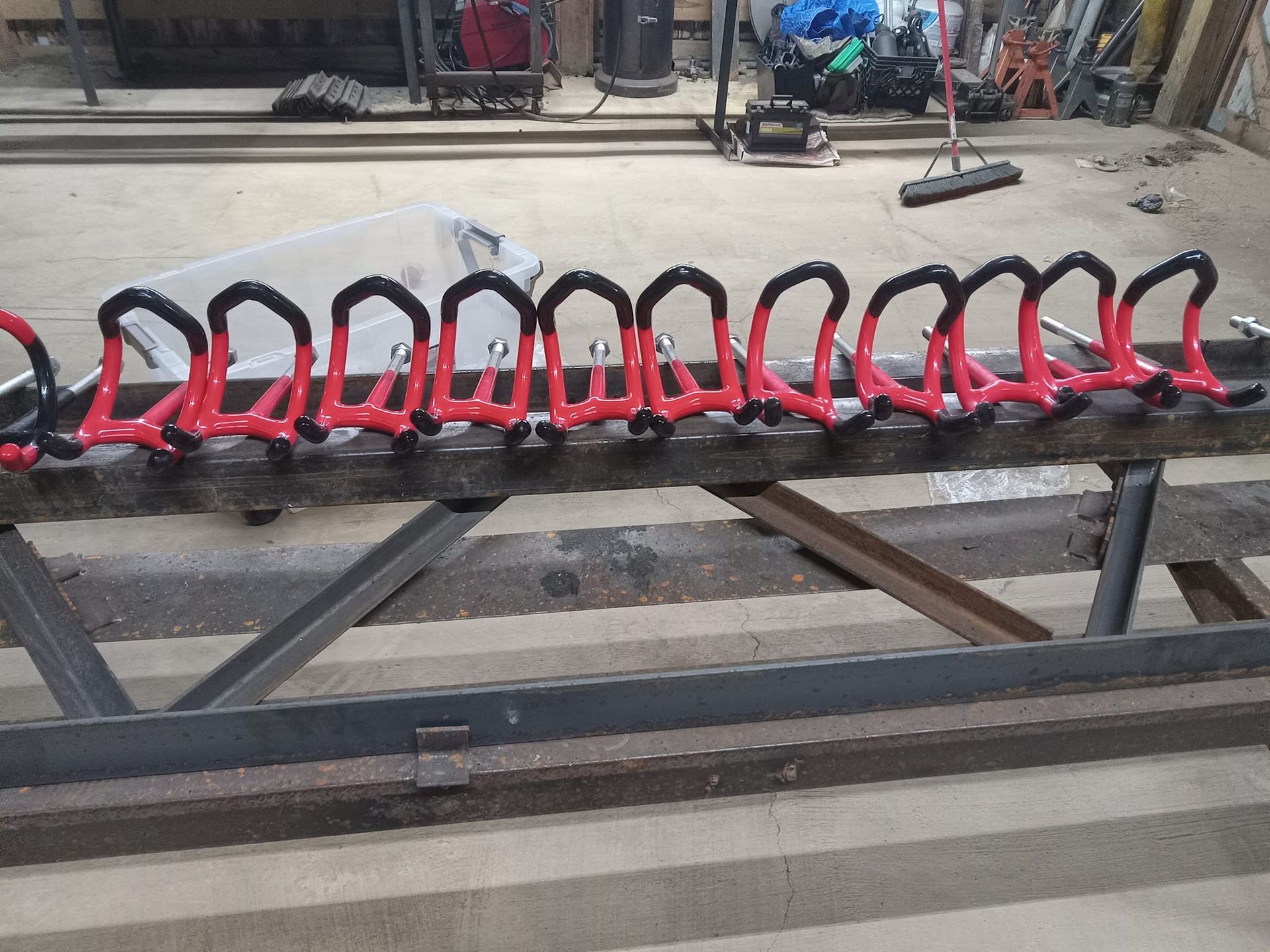 Red metal hooks lined up on a metal beam in a workshop.