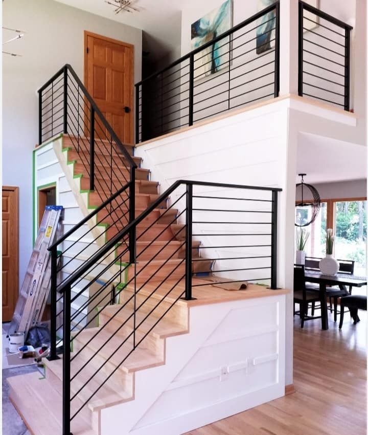 Modern staircase with black metal railings, light wood steps and flooring, white walls.