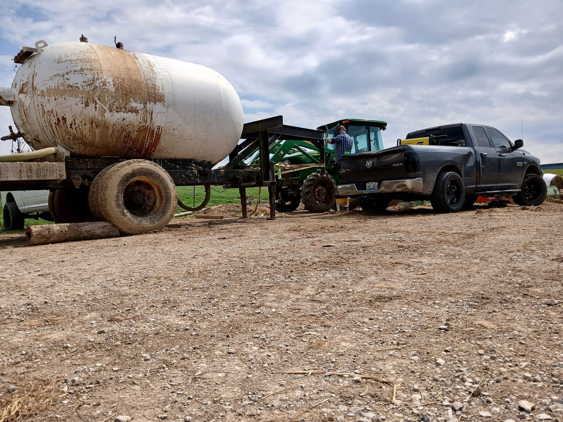 A pickup truck, tractor, and propane tank on a gravel road, likely in a rural setting.