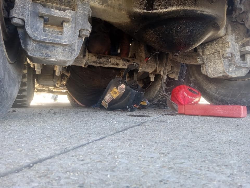 Person working on the underside of a truck on a paved surface, red tool visible.