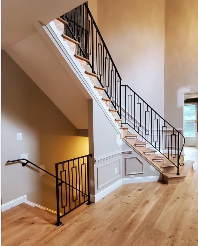 Wooden staircase with black metal railing, leading upwards. Light wood flooring and neutral wall colors.