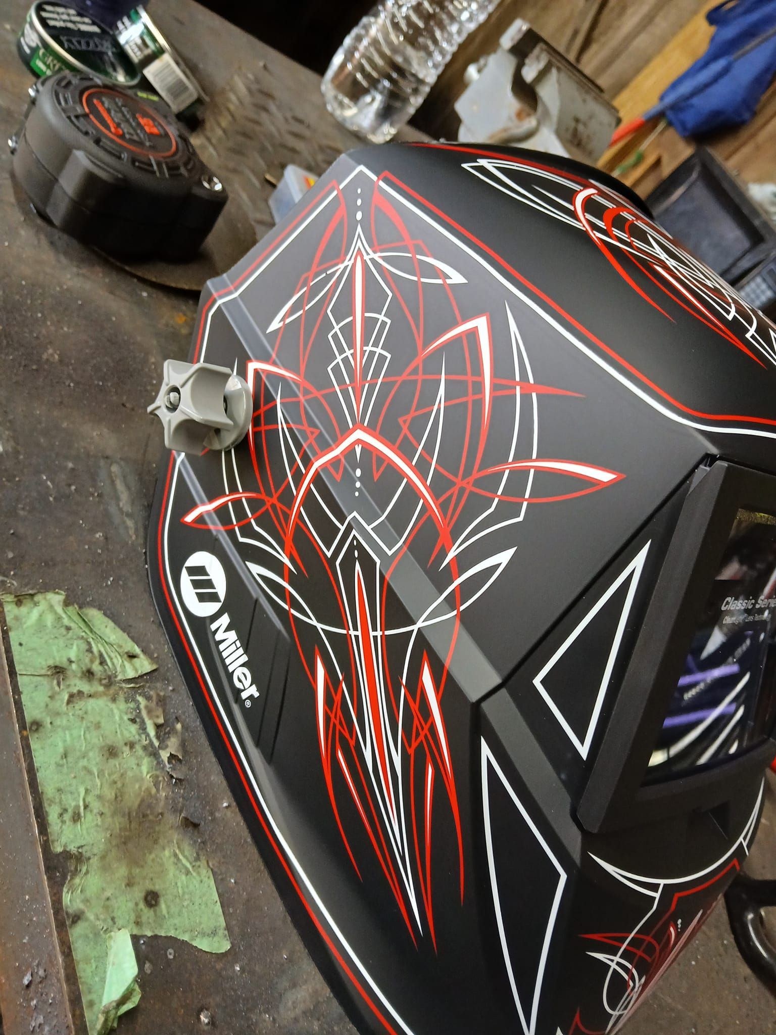 Black Miller welding helmet with red and white pinstriping, sitting on a metal surface.