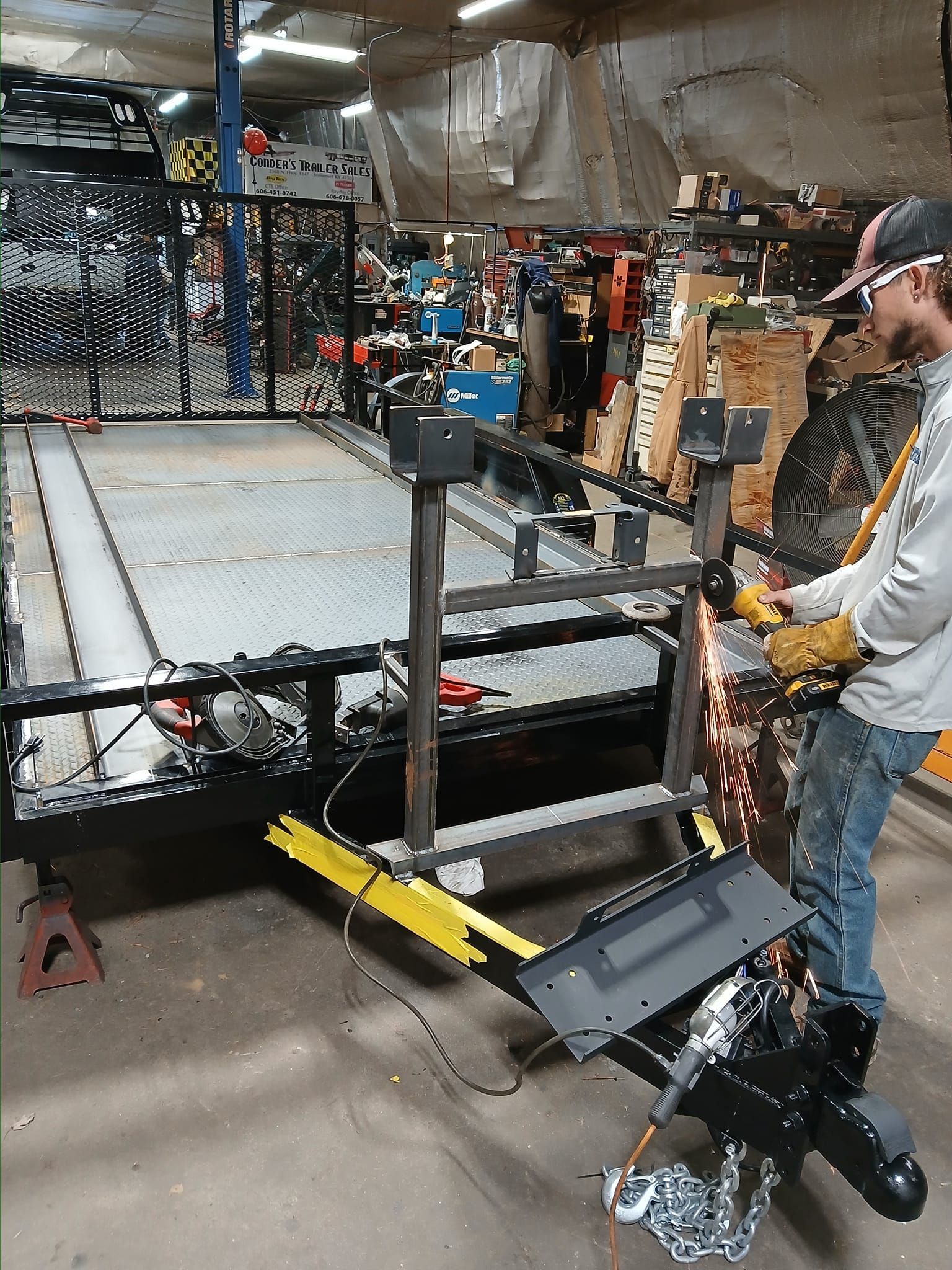 Man using grinder on metal trailer in a workshop, sparks flying.