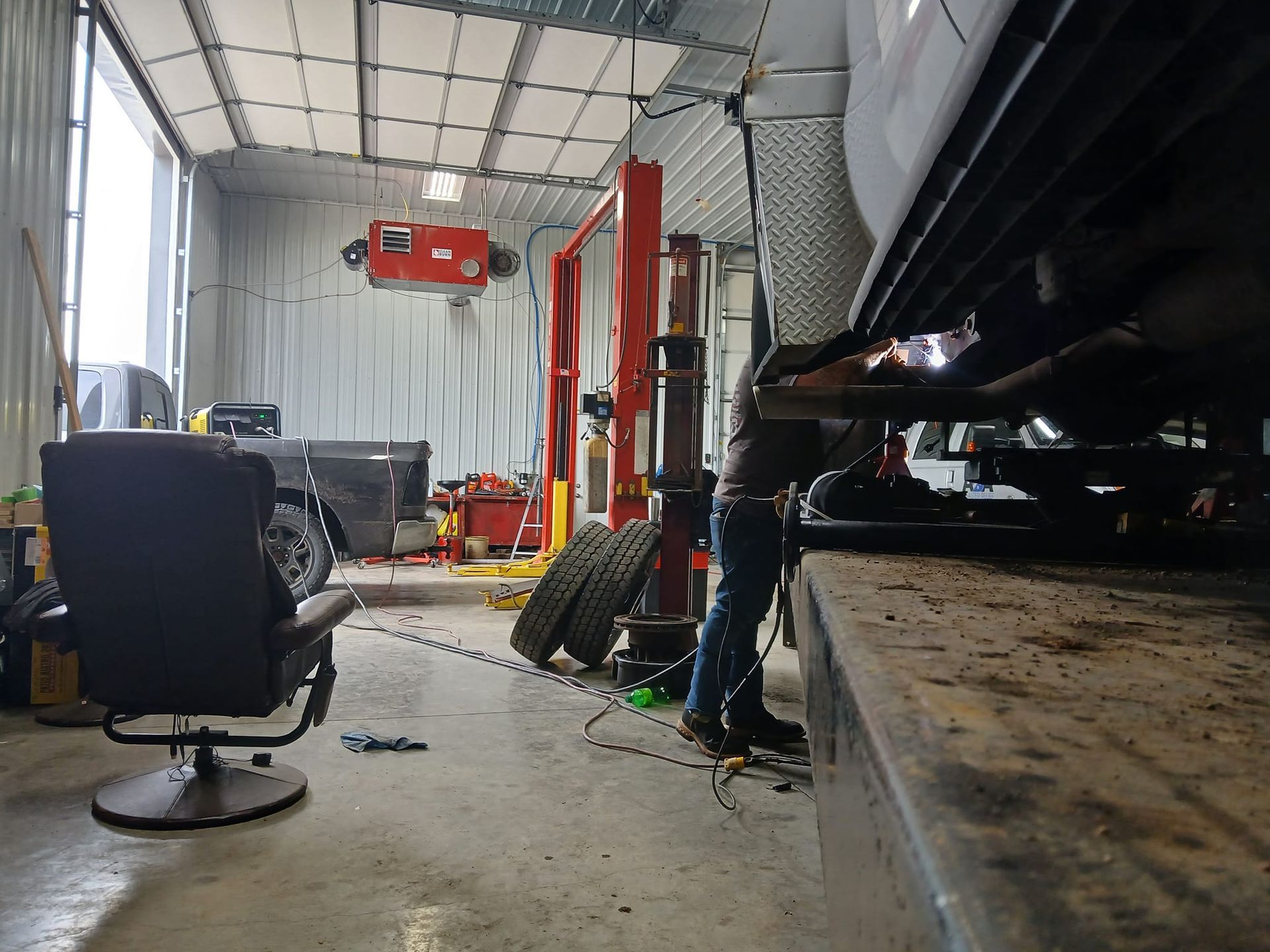 A mechanic working under a vehicle raised on a lift inside a garage.