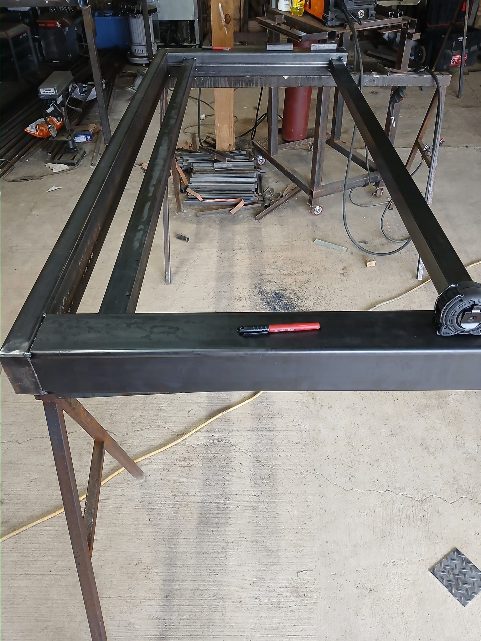 Metal frame construction in a workshop, possibly for a large project, with a sawhorse supporting it.