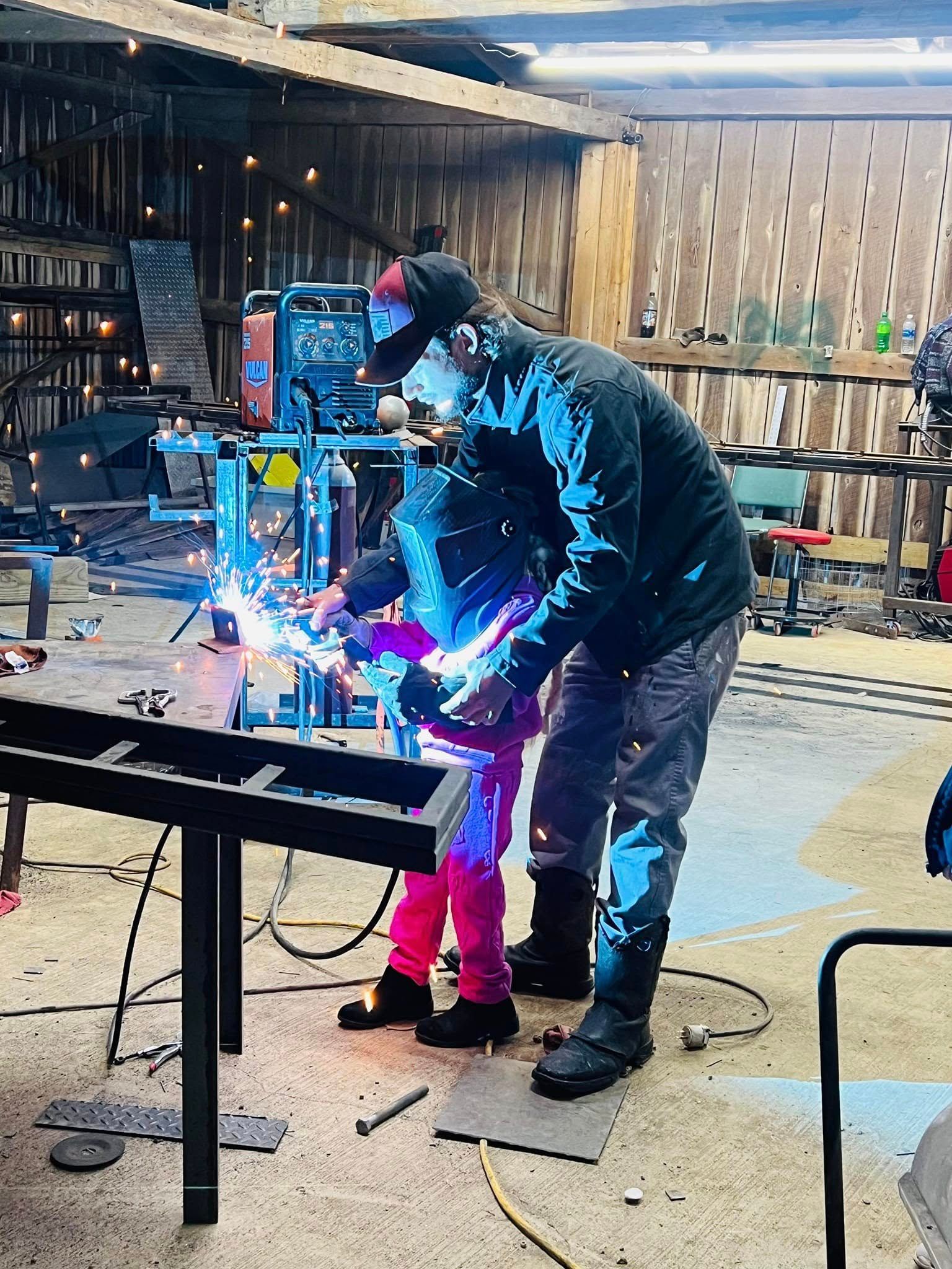 Man and child welding metal in workshop, sparks flying.