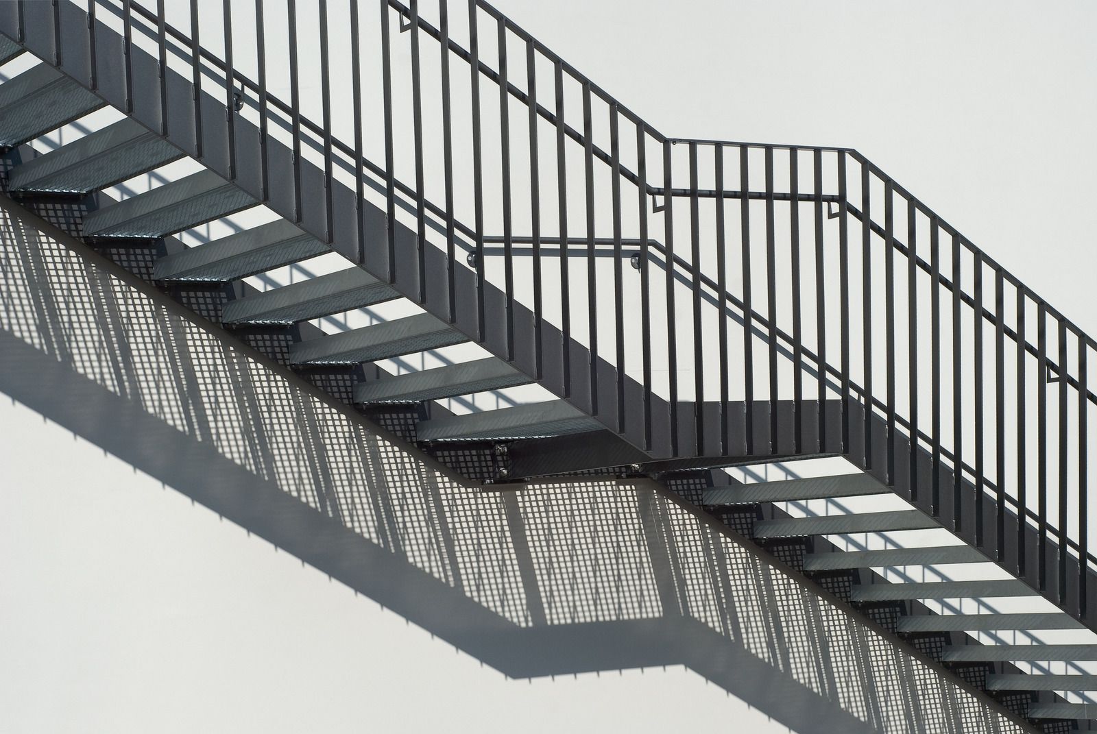 Metal fire escape stairs cast shadow on white wall.