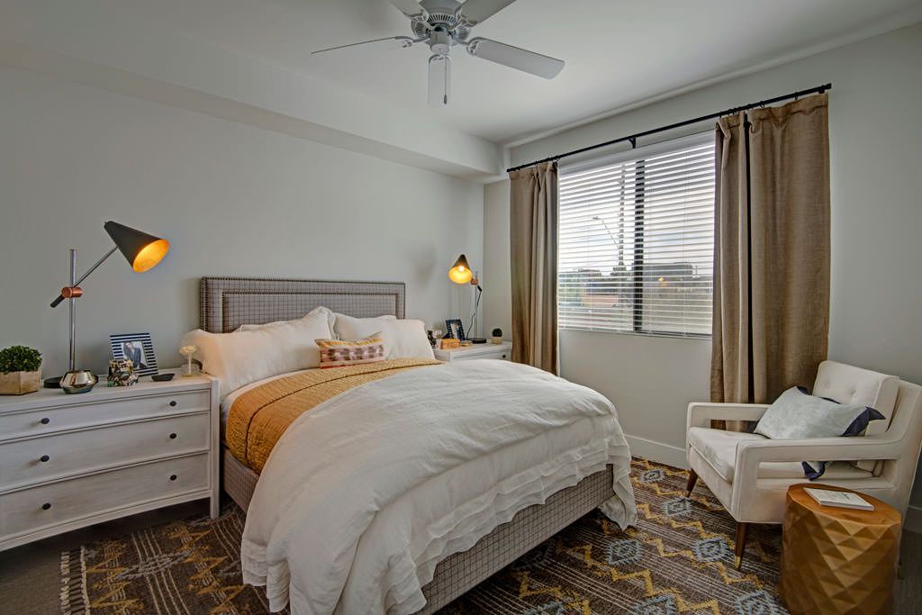 A bedroom with a bed , chair , dresser and ceiling fan.