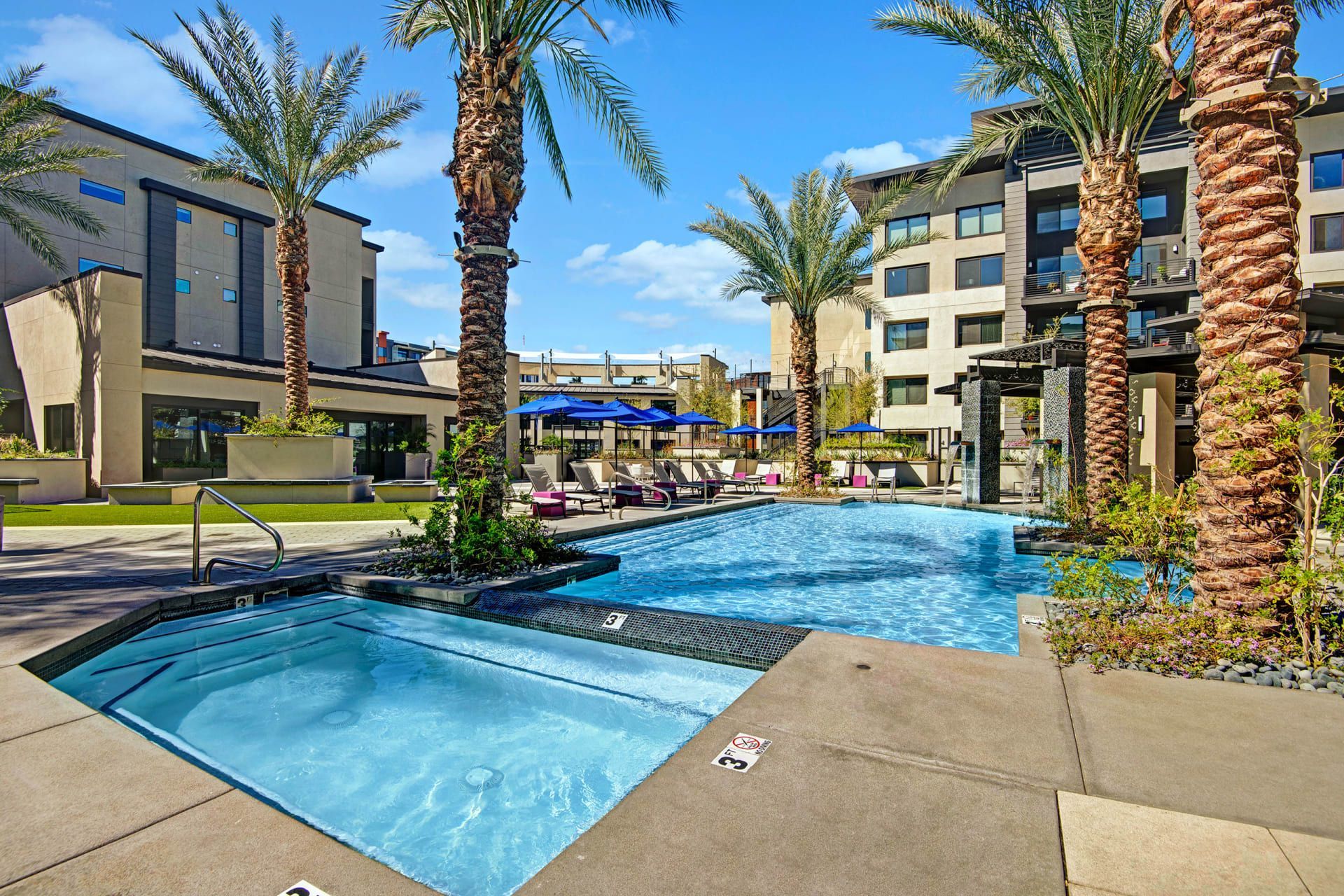 A large swimming pool with palm trees in front of a building.