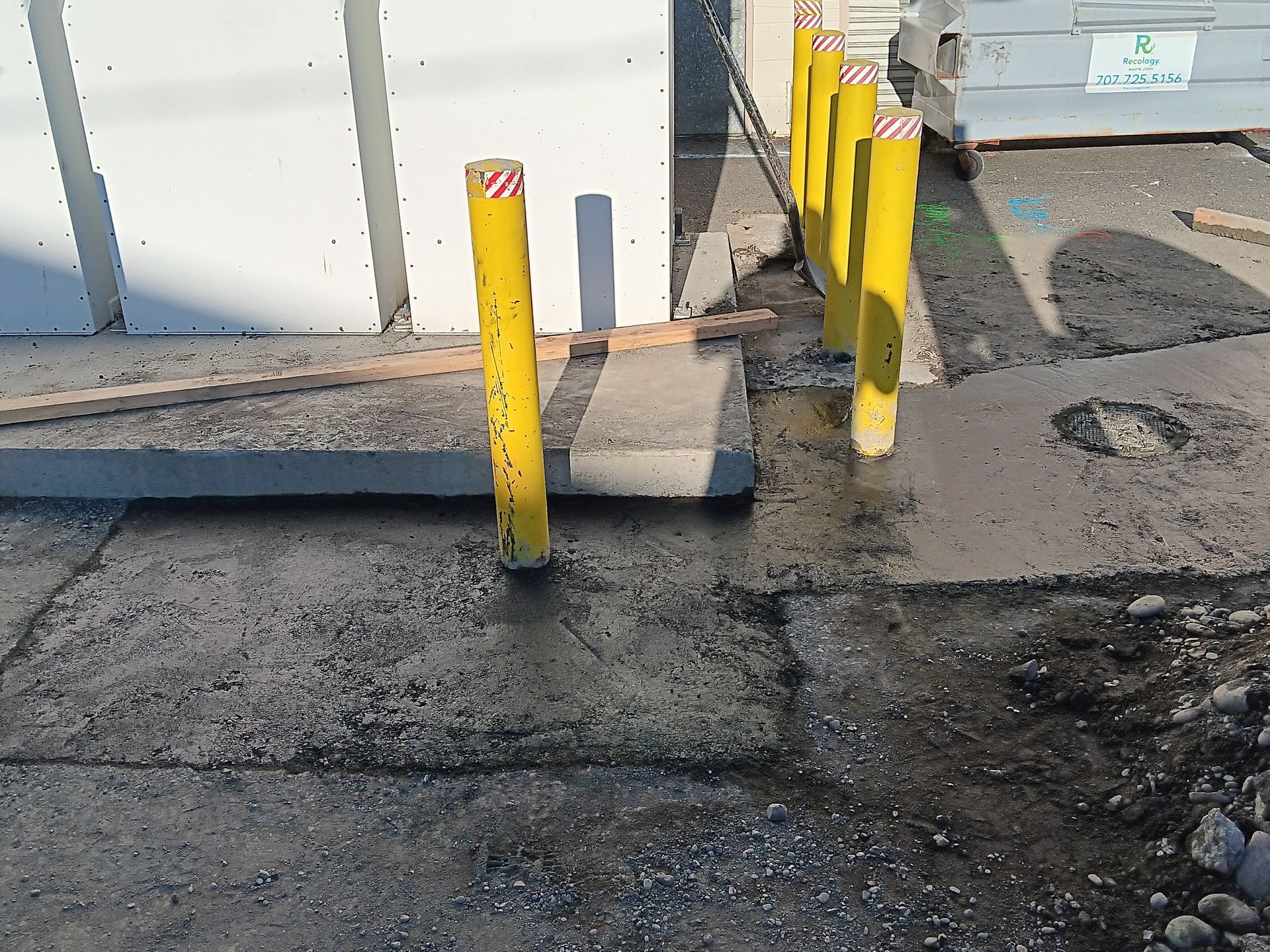 Yellow bollards beside a building on a rough, muddy sidewalk with a damaged curb ramp