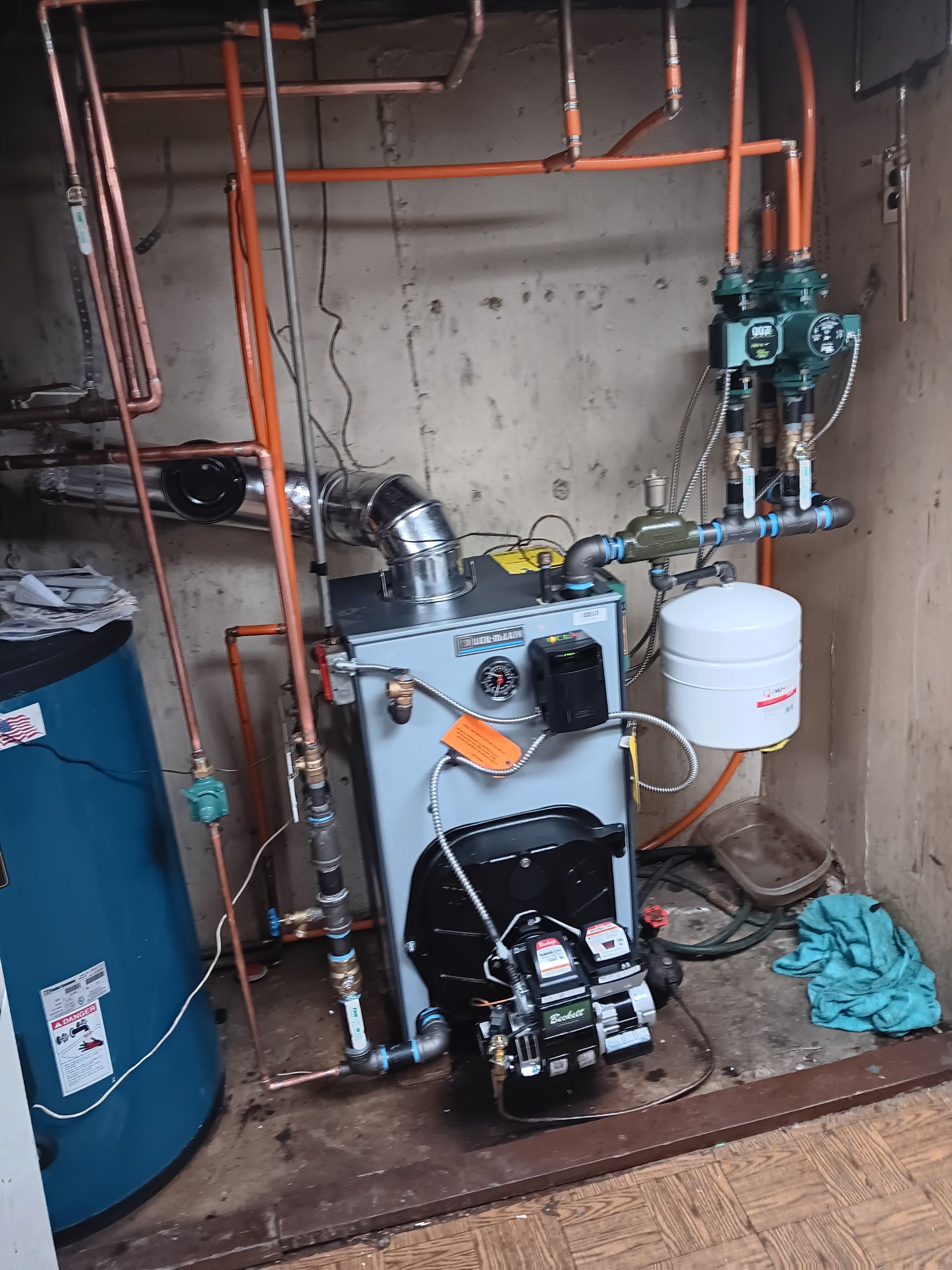 Basement utility room with water heater, boiler, pipes, and valves mounted on a concrete wall.