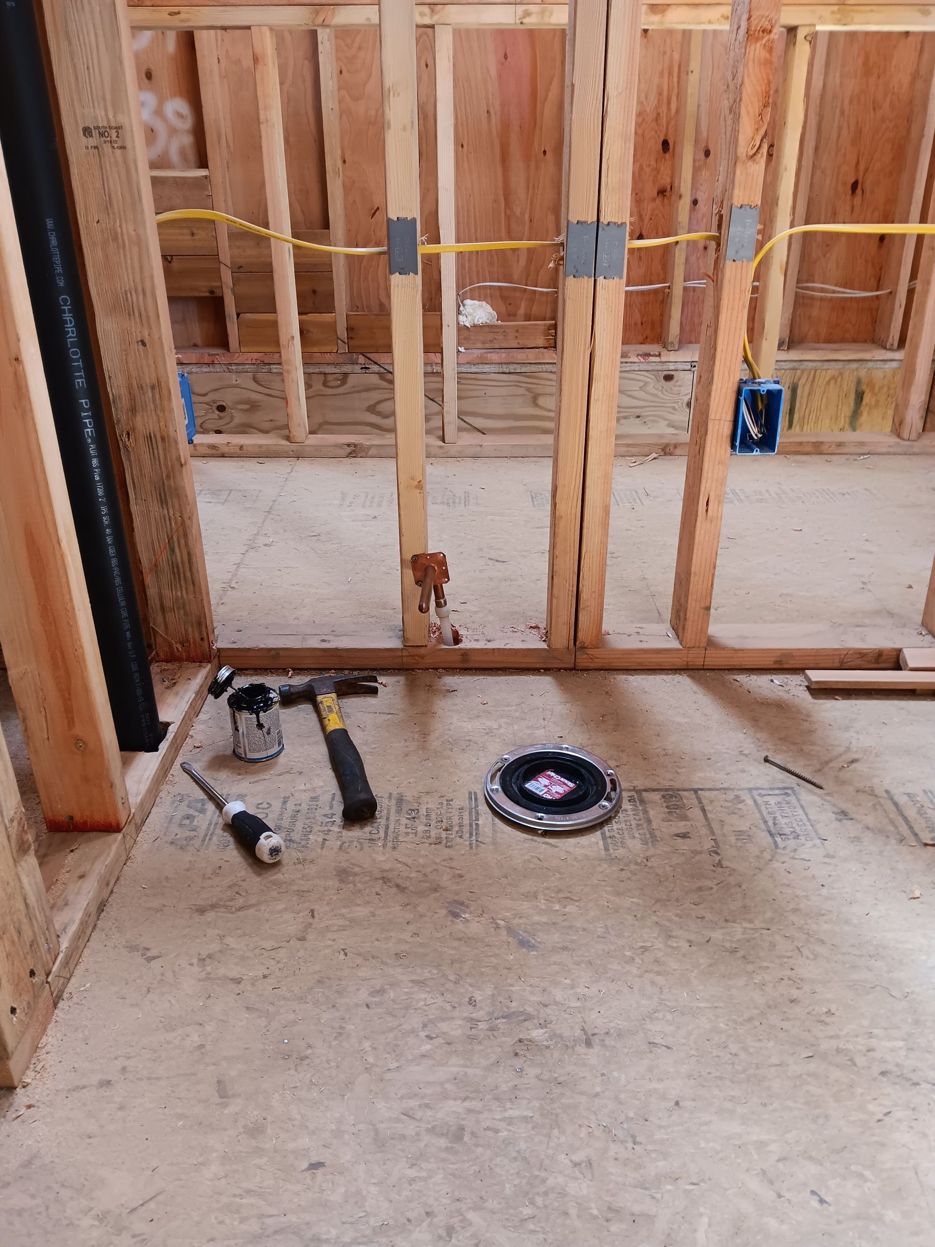 Partially framed room with exposed wall studs, tools on the subfloor, and a circular saw blade on the floor