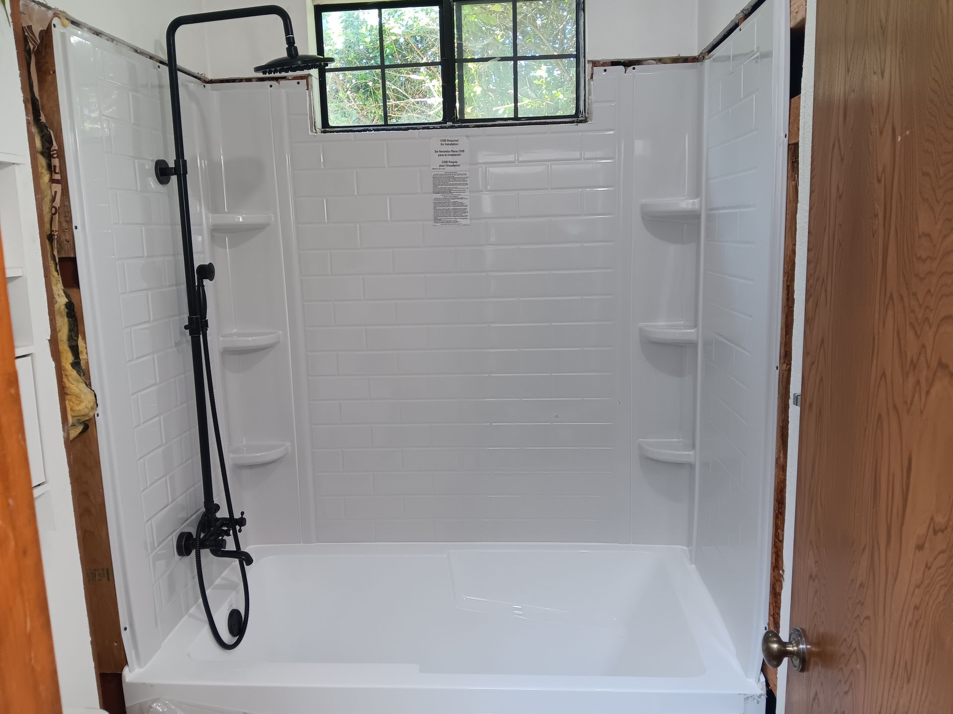 Walk-in shower with white tile, built-in shelves, black showerhead, and a window above the tub.