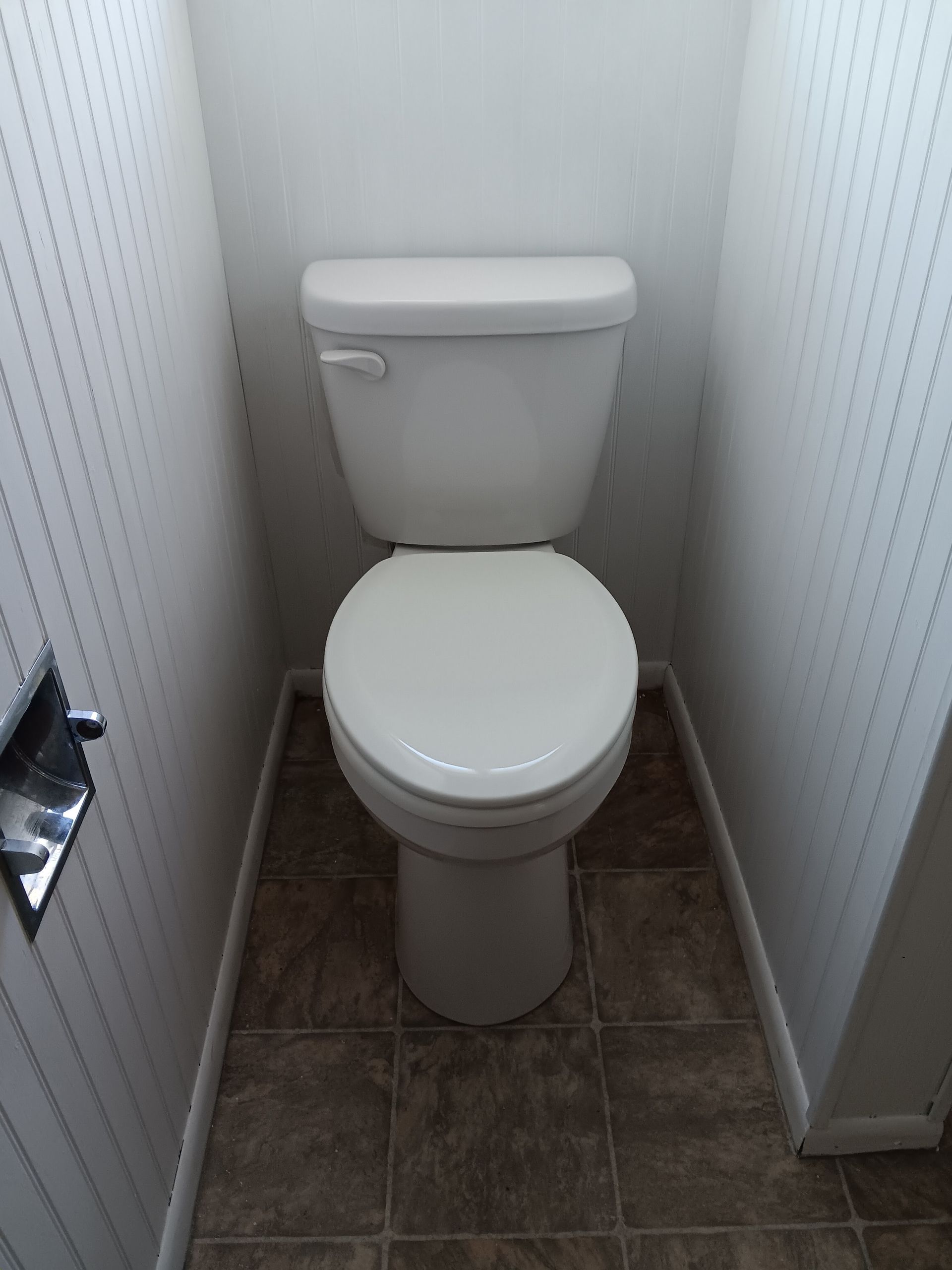Small bathroom with a white toilet centered between narrow tiled walls.