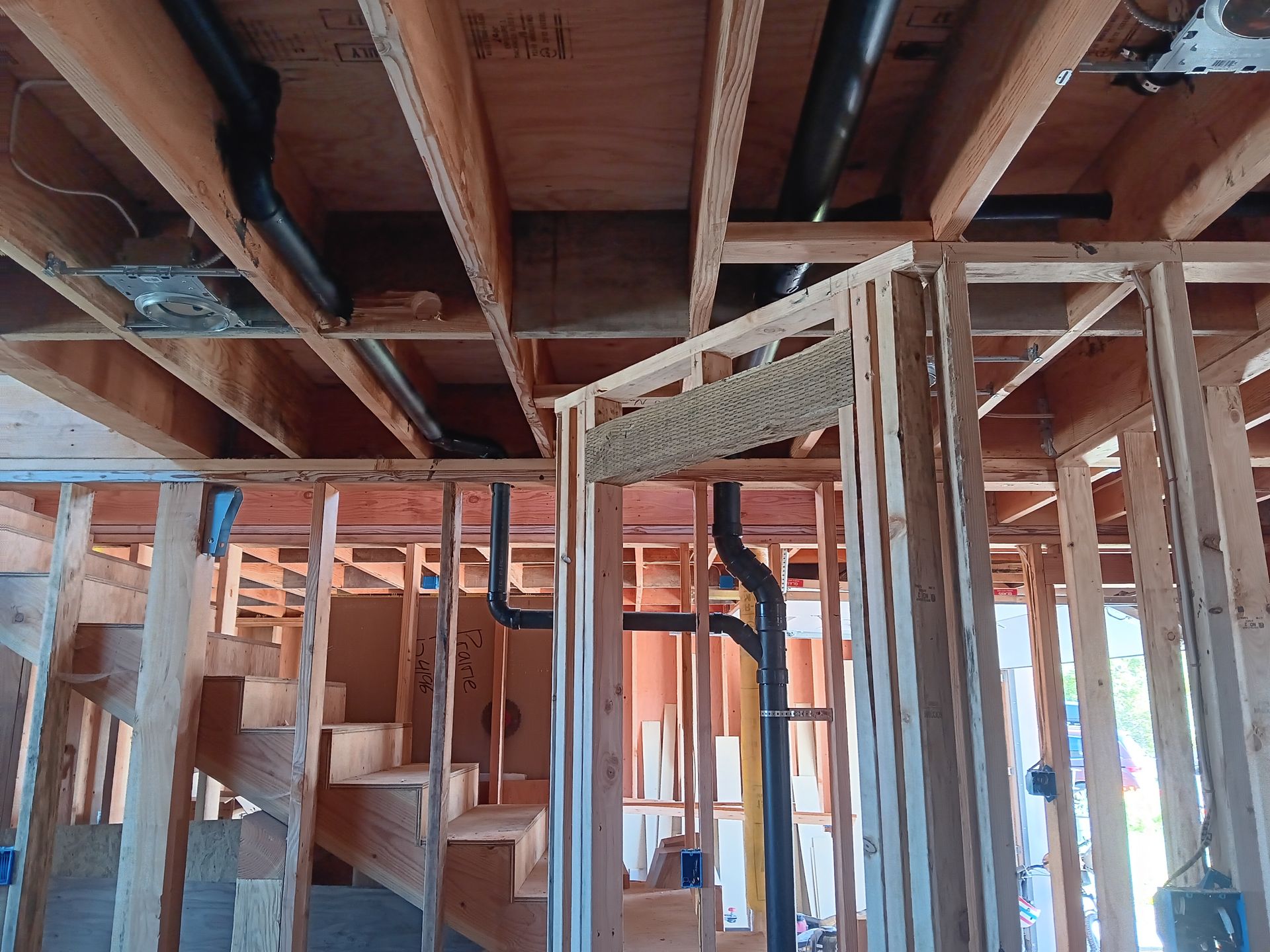 The inside of a house under construction with stairs and pipes.