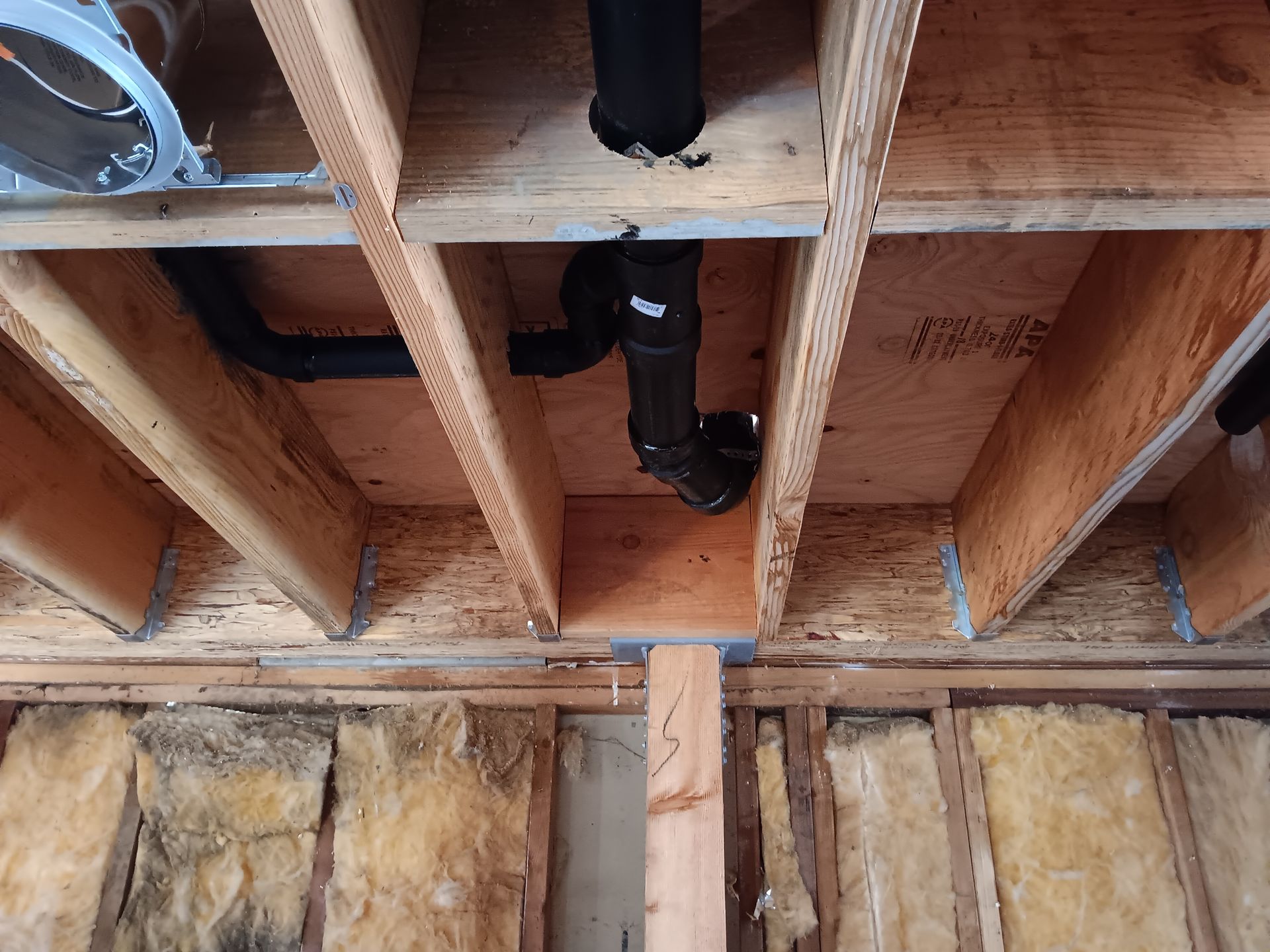 Exposed attic ceiling framing with black plumbing pipes and insulation below