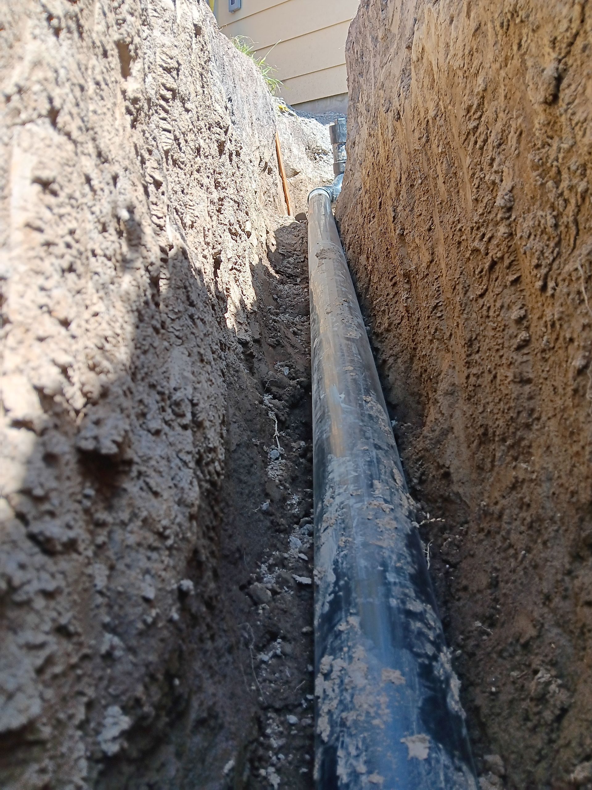 Trench with a large pipe channeling water between dirt walls outdoors