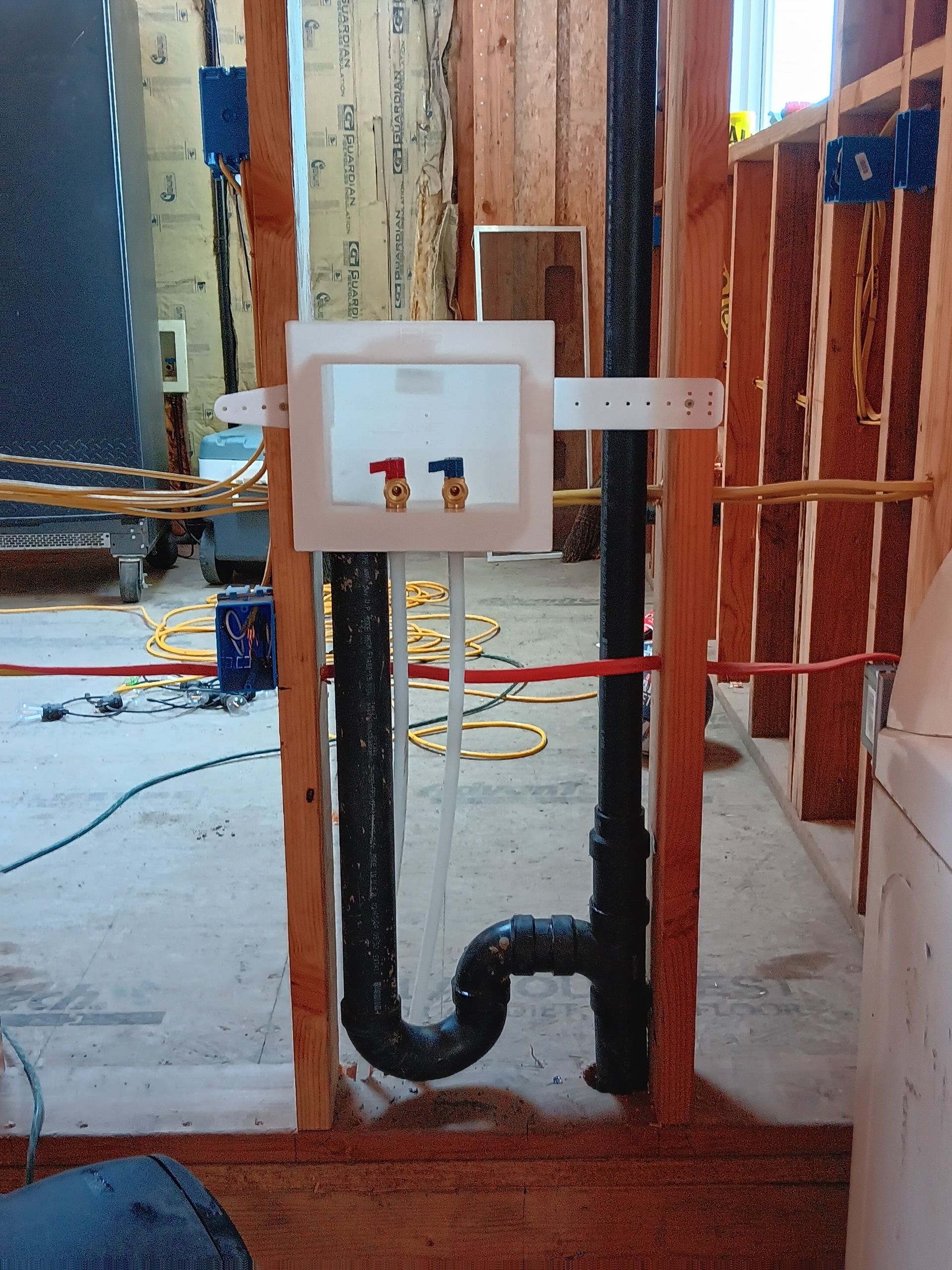 In-wall plumbing rough-in with white inspection box, black drain pipe, and exposed wooden framing.