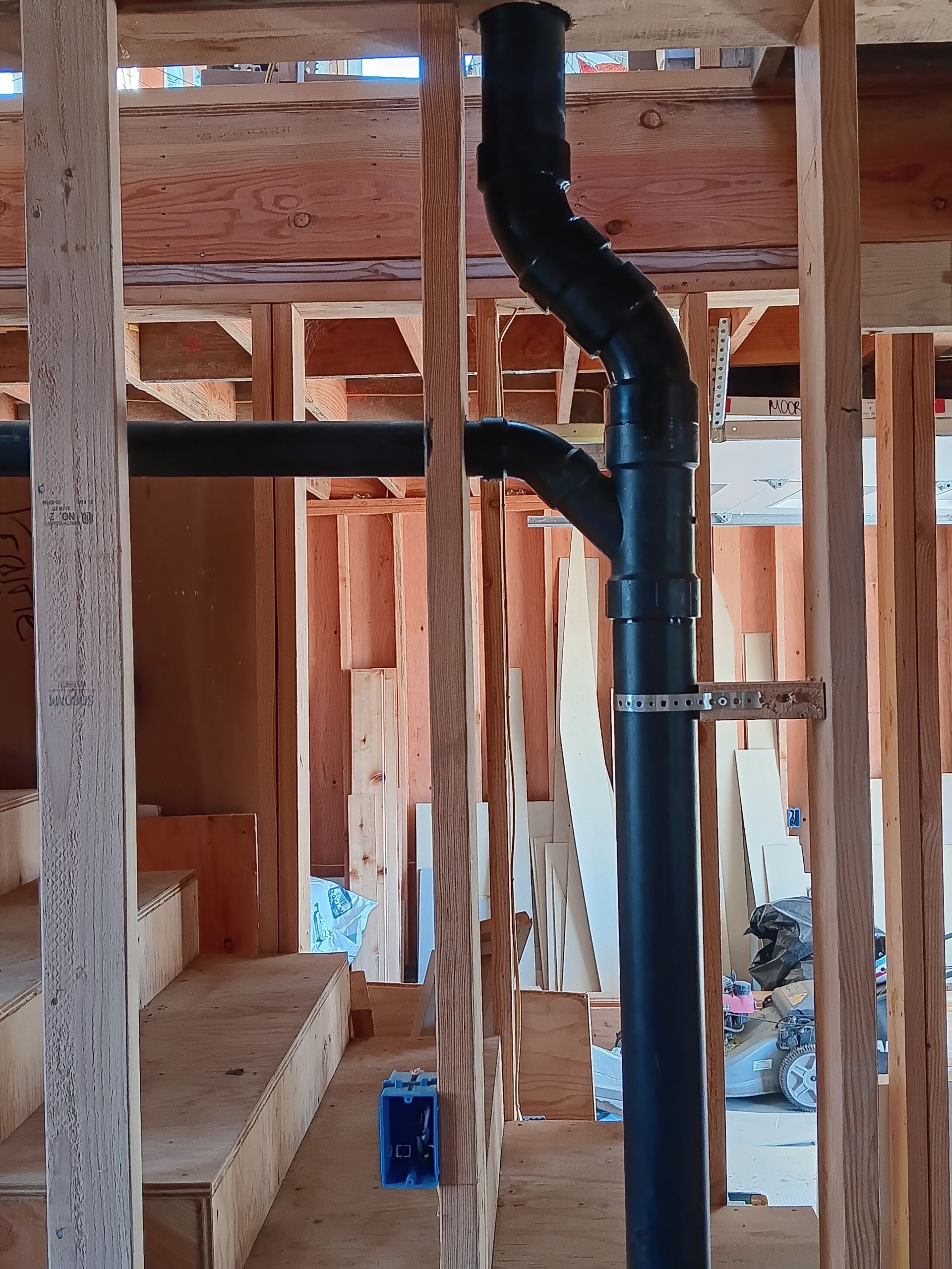 Black plumbing pipe running through exposed wooden framing inside a house under construction