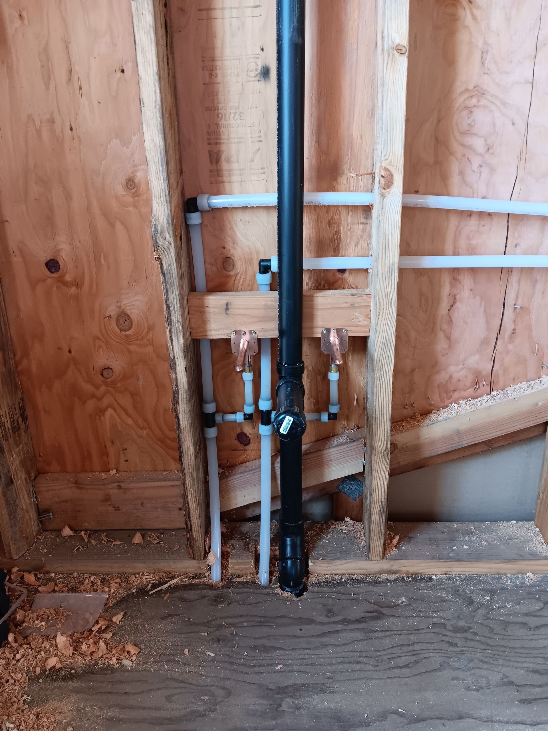 Plumbing pipes and valves installed against unfinished plywood wall in a utility area