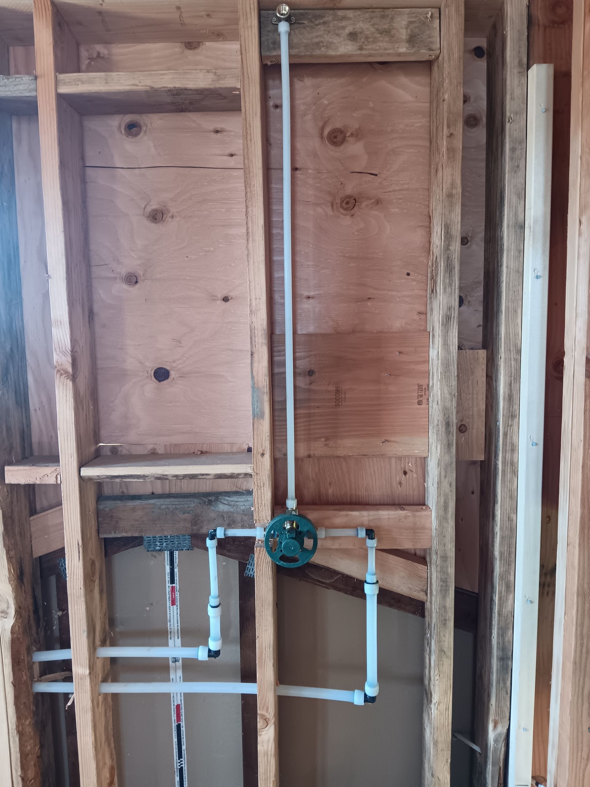 Exposed wall framing with plumbing pipes and a valve in an unfinished room