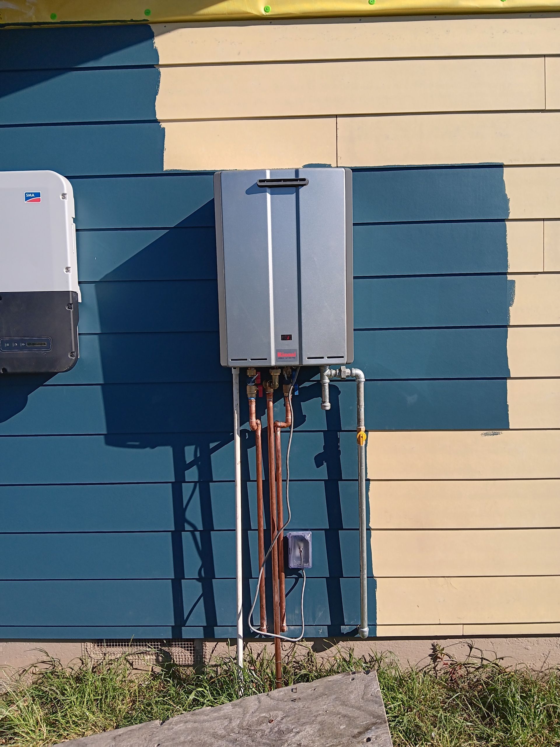 Two gray utility boxes mounted on a blue-and-beige building wall with pipes below