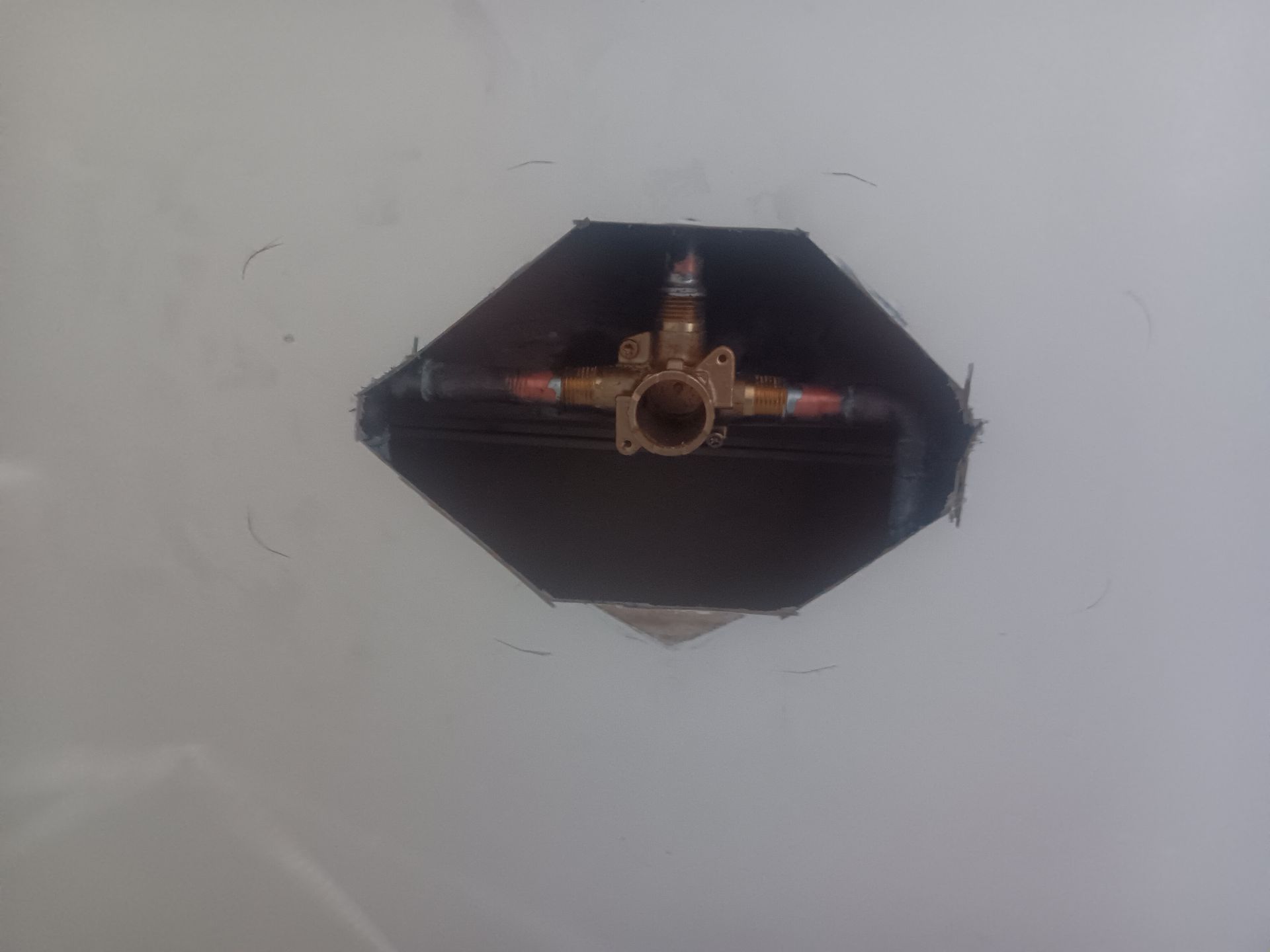 Wall-mounted metal valve inside a dark octagonal opening on a white wall.