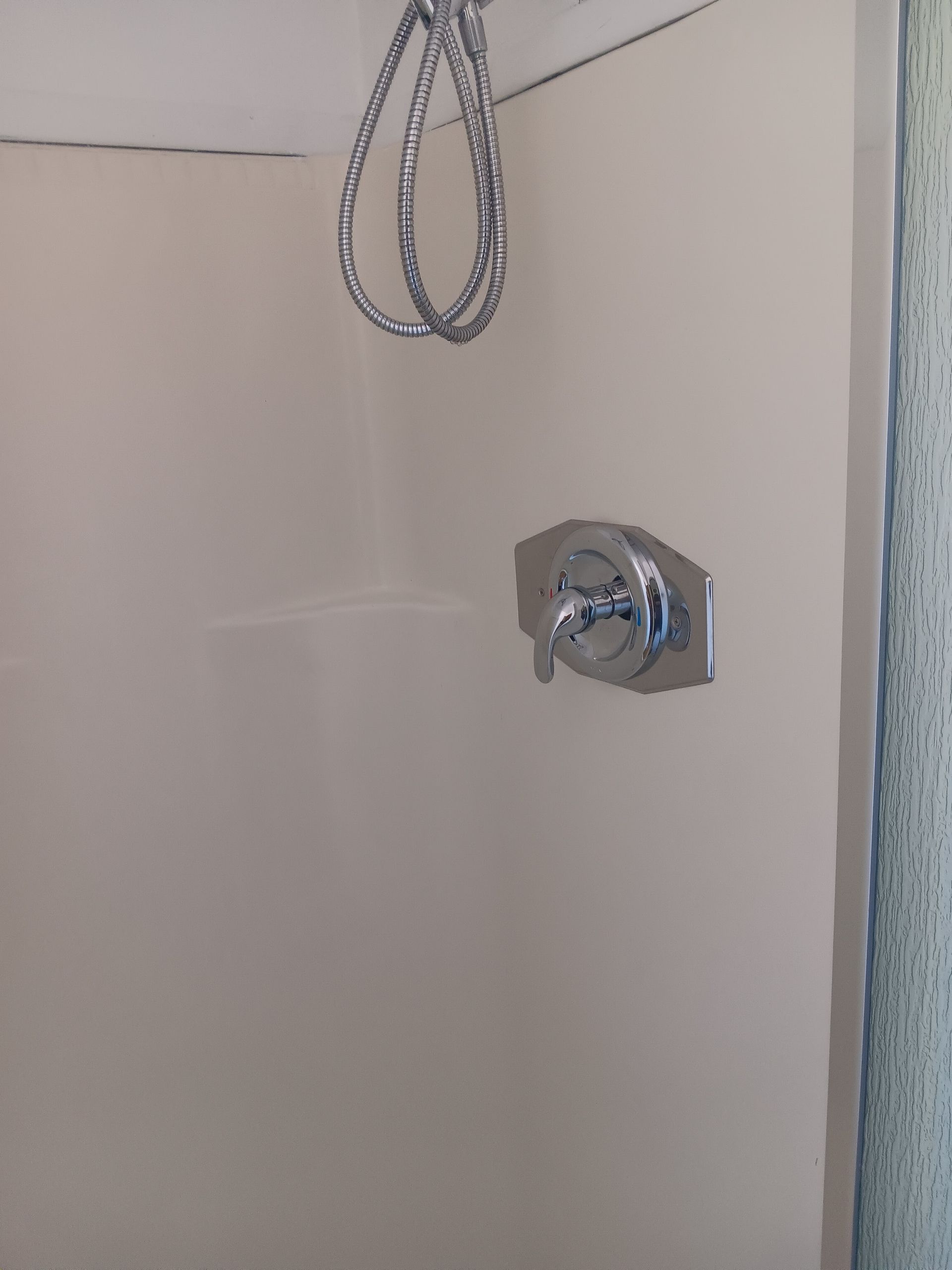 Small white bathroom wall with a chrome shower control and a hanging chain or cord near the ceiling.