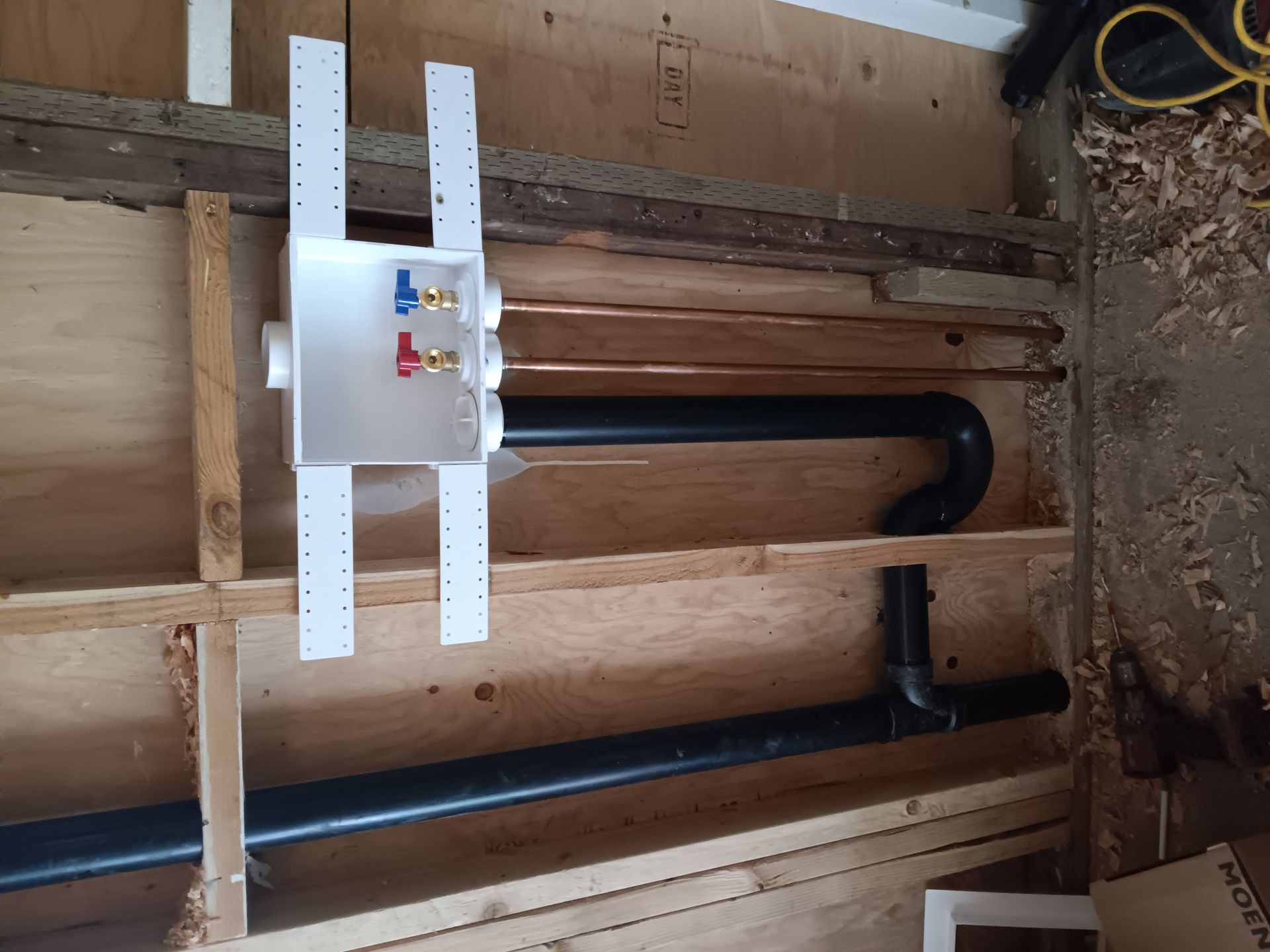 Wall-mounted plumbing pipes and a white valve box inside an unfinished room.