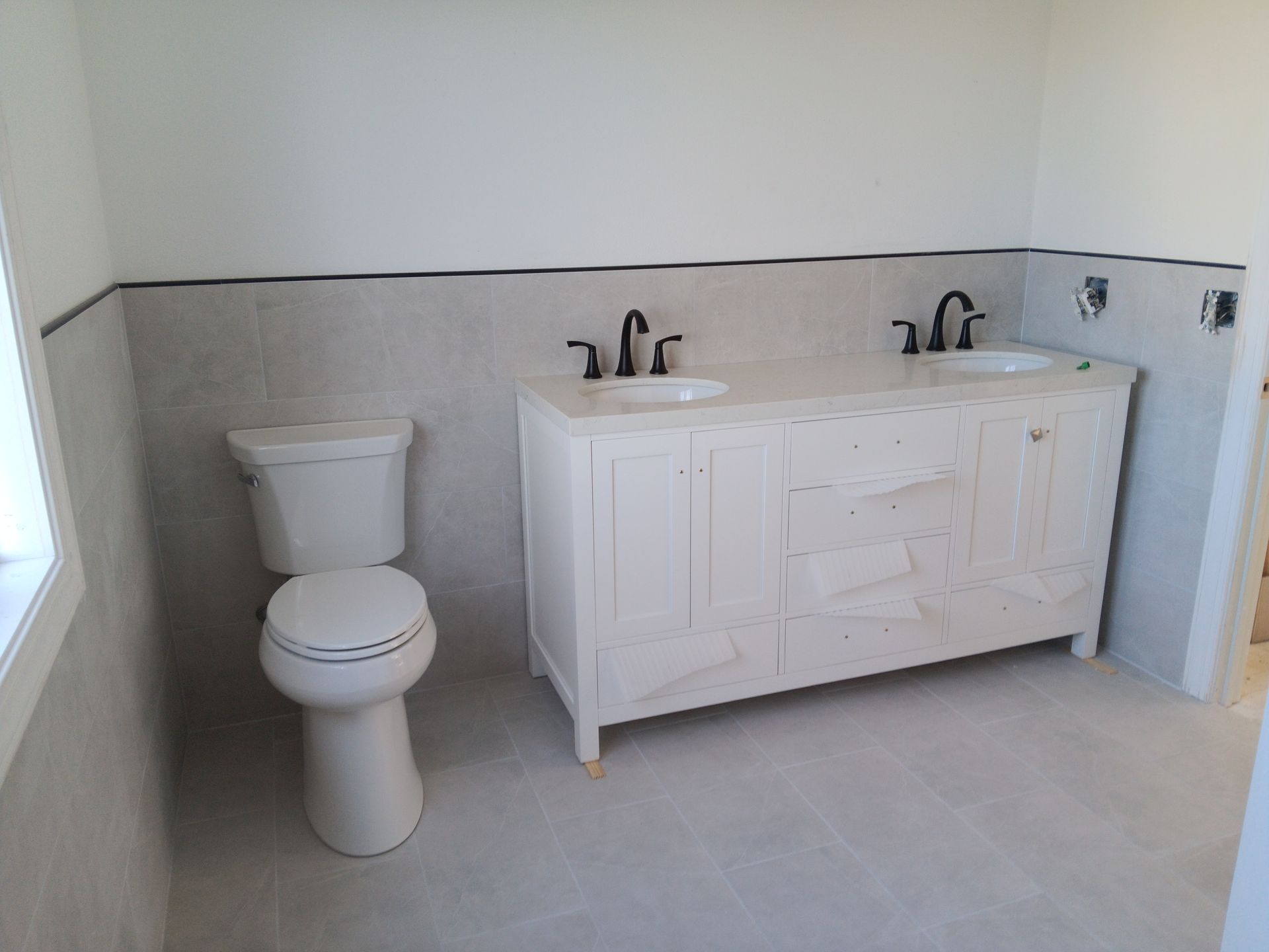 Bathroom with white toilet and white double vanity sink against gray walls and floor
