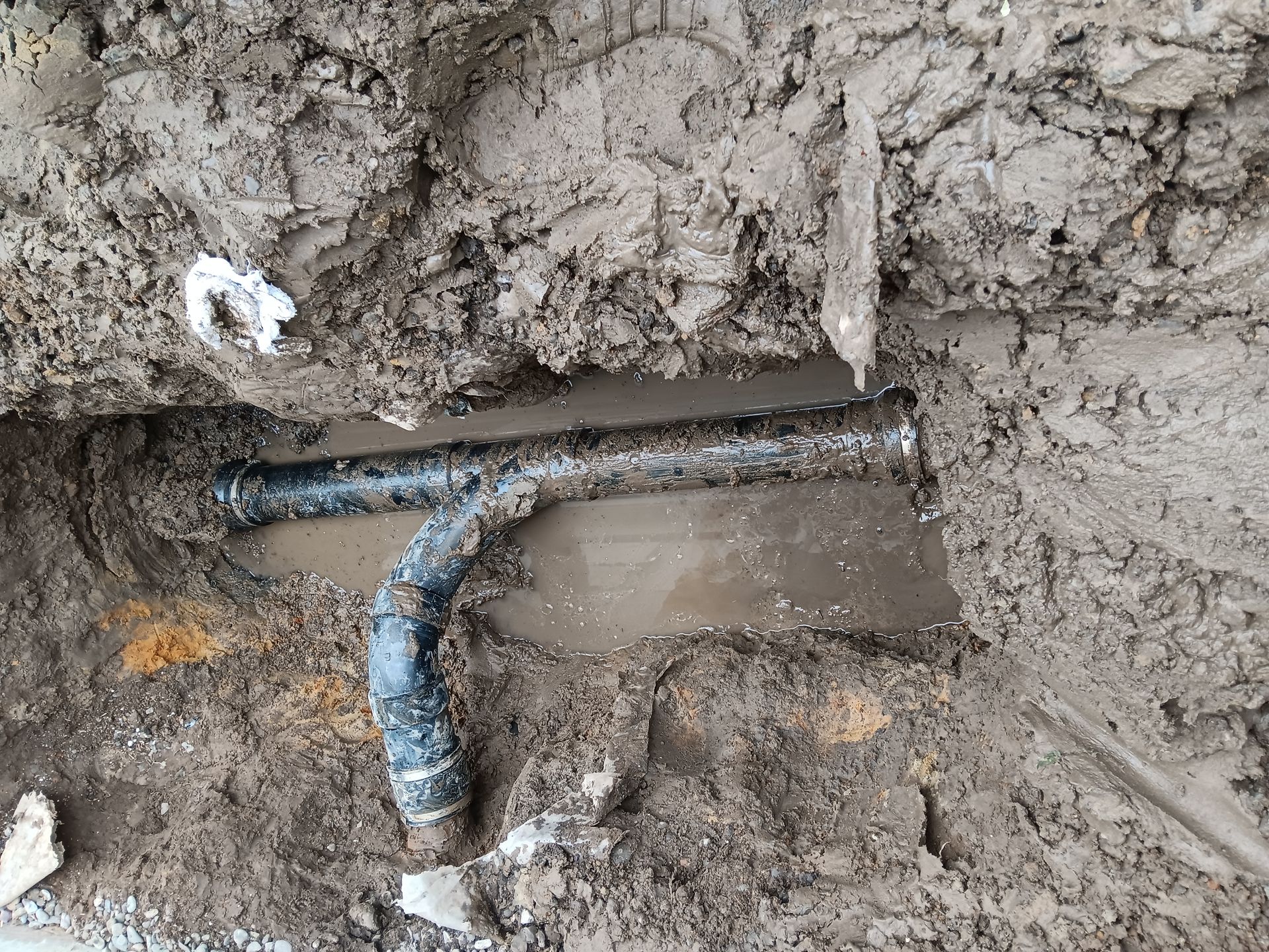 Exposed underground pipe with a blue elbow joint in muddy soil and dirt trench