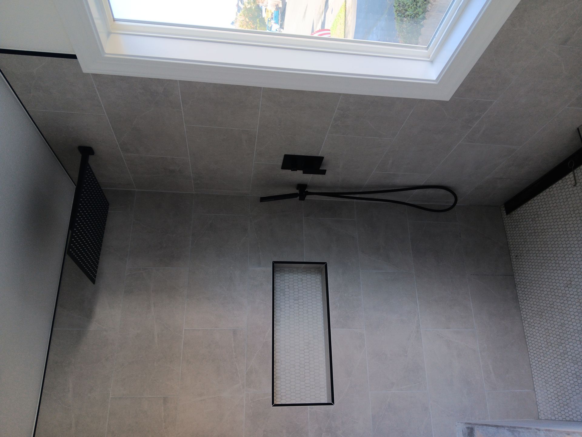 Gray tiled shower with a skylight, black showerhead, and rectangular recessed niche on the wall