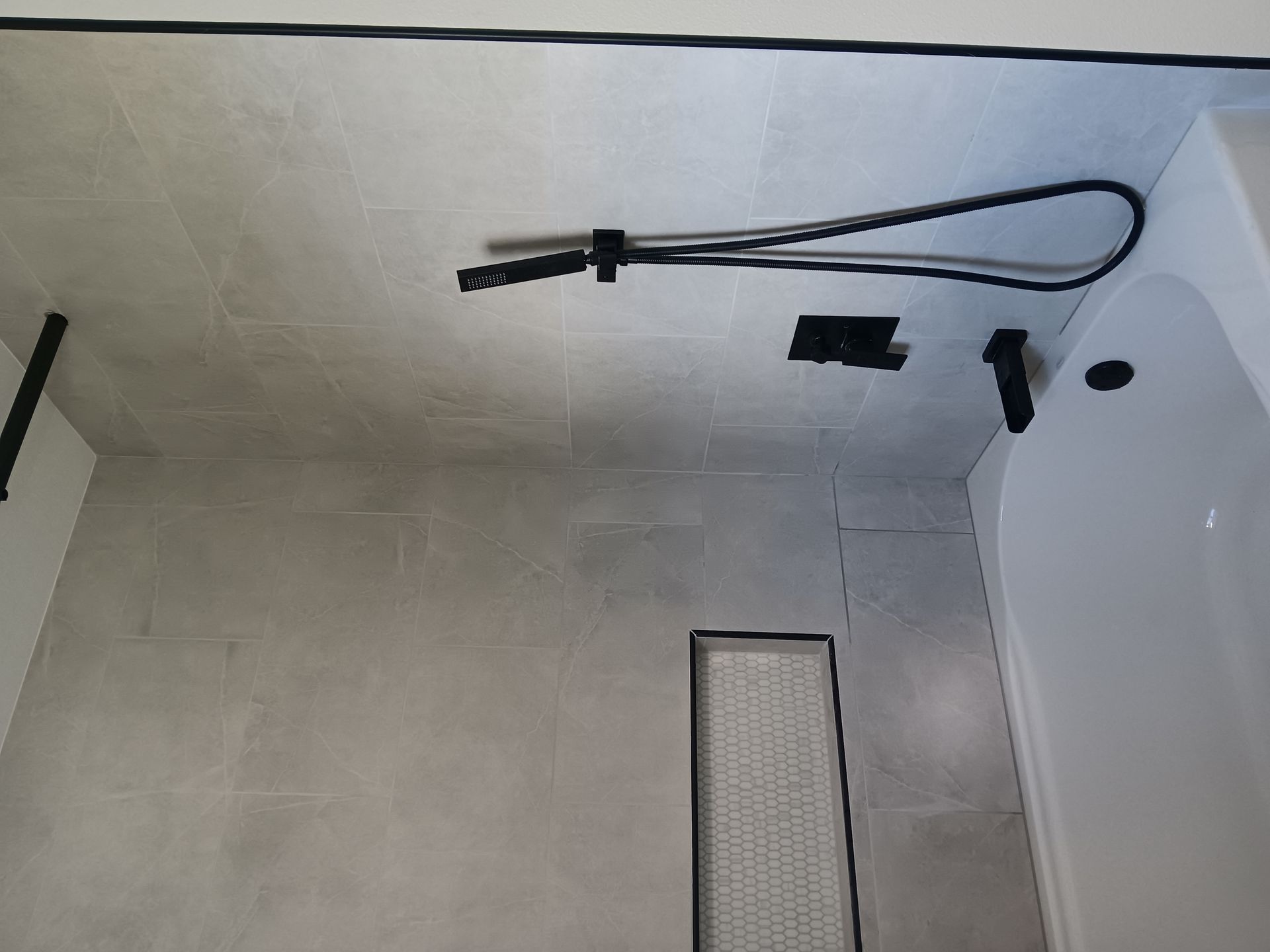 Modern bathroom shower area with gray tile, handheld shower hose, and built-in floor drain channel