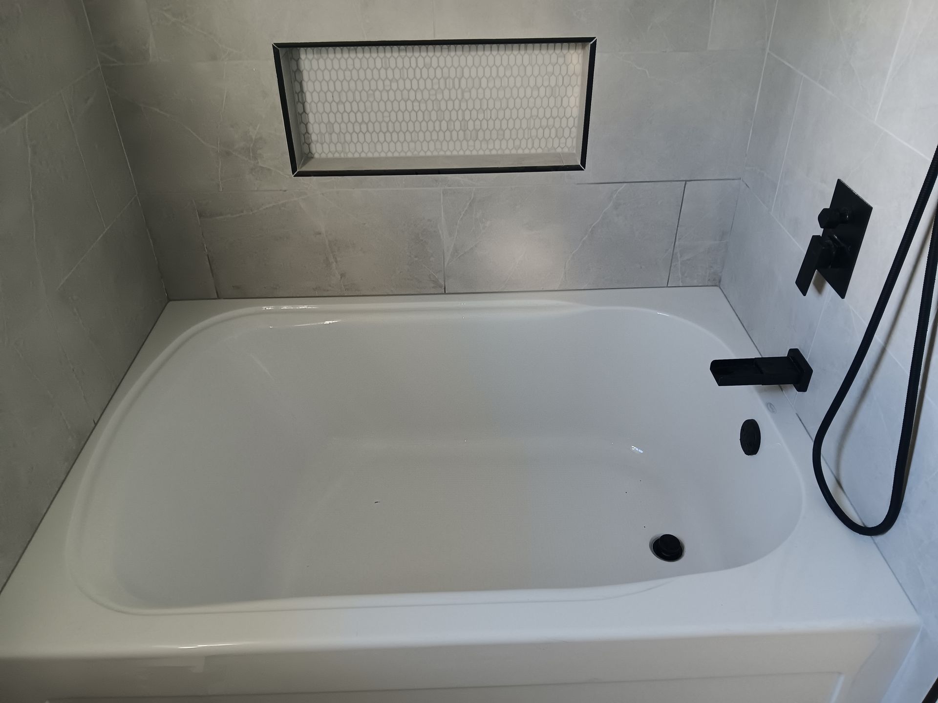 White bathtub with black fixtures in a tiled bathroom.