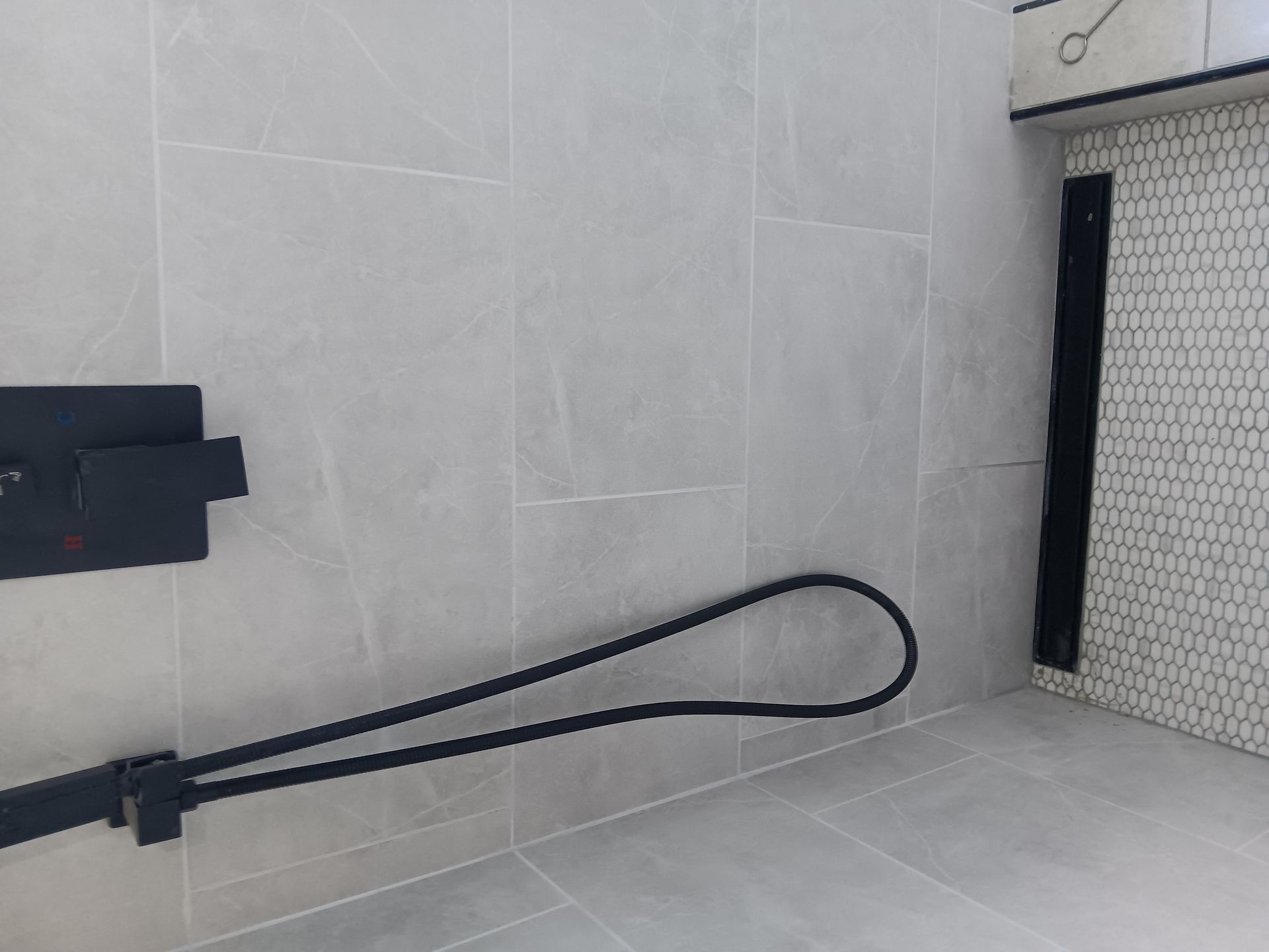 Black strap or cable loop on a light gray tiled floor beside a wall.