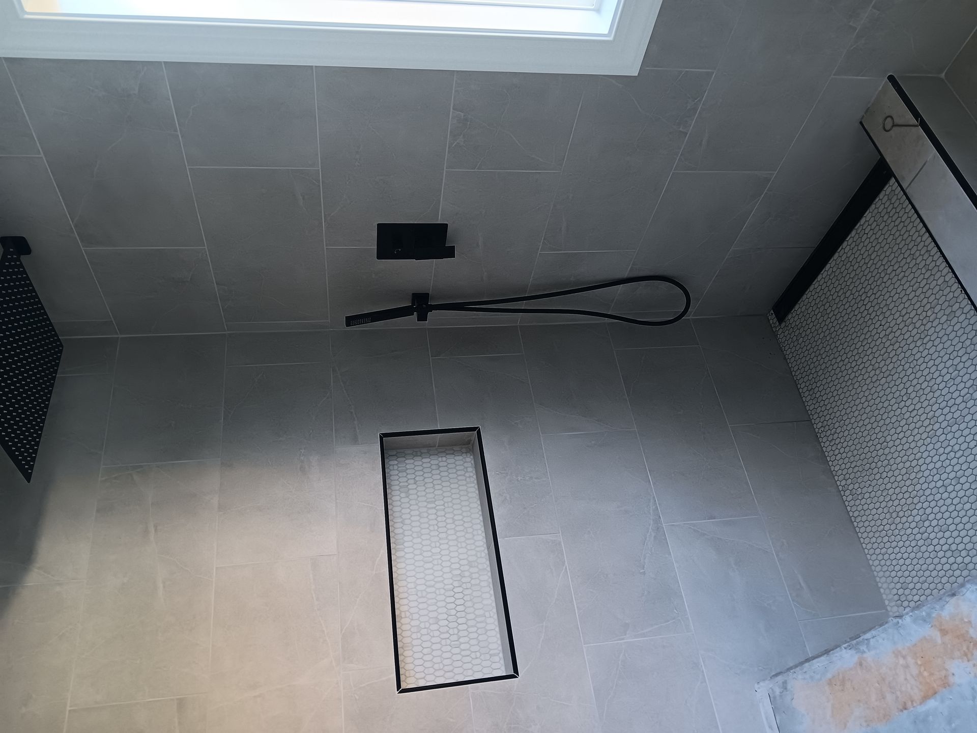 Empty gray tiled shower stall with a window and built-in shelf or niche.