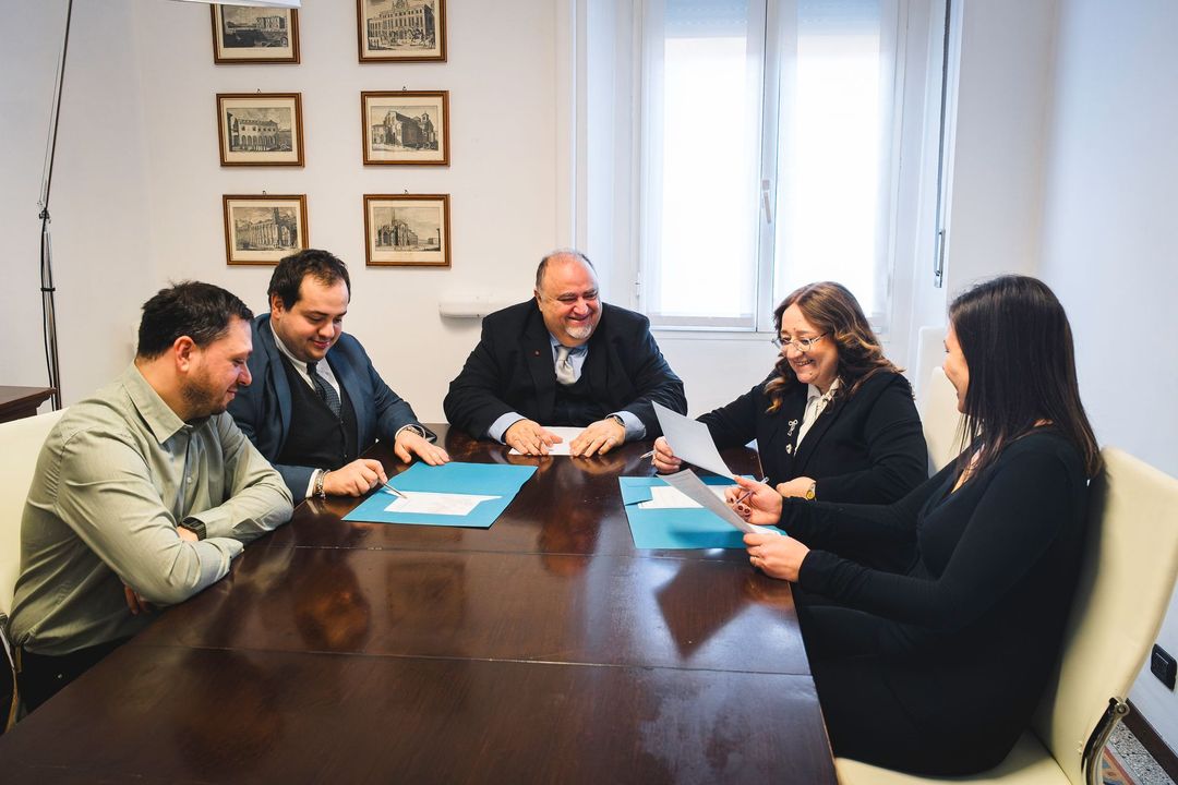 Cinque persone sedute a un tavolo di legno in un ufficio, rivolte in avanti.