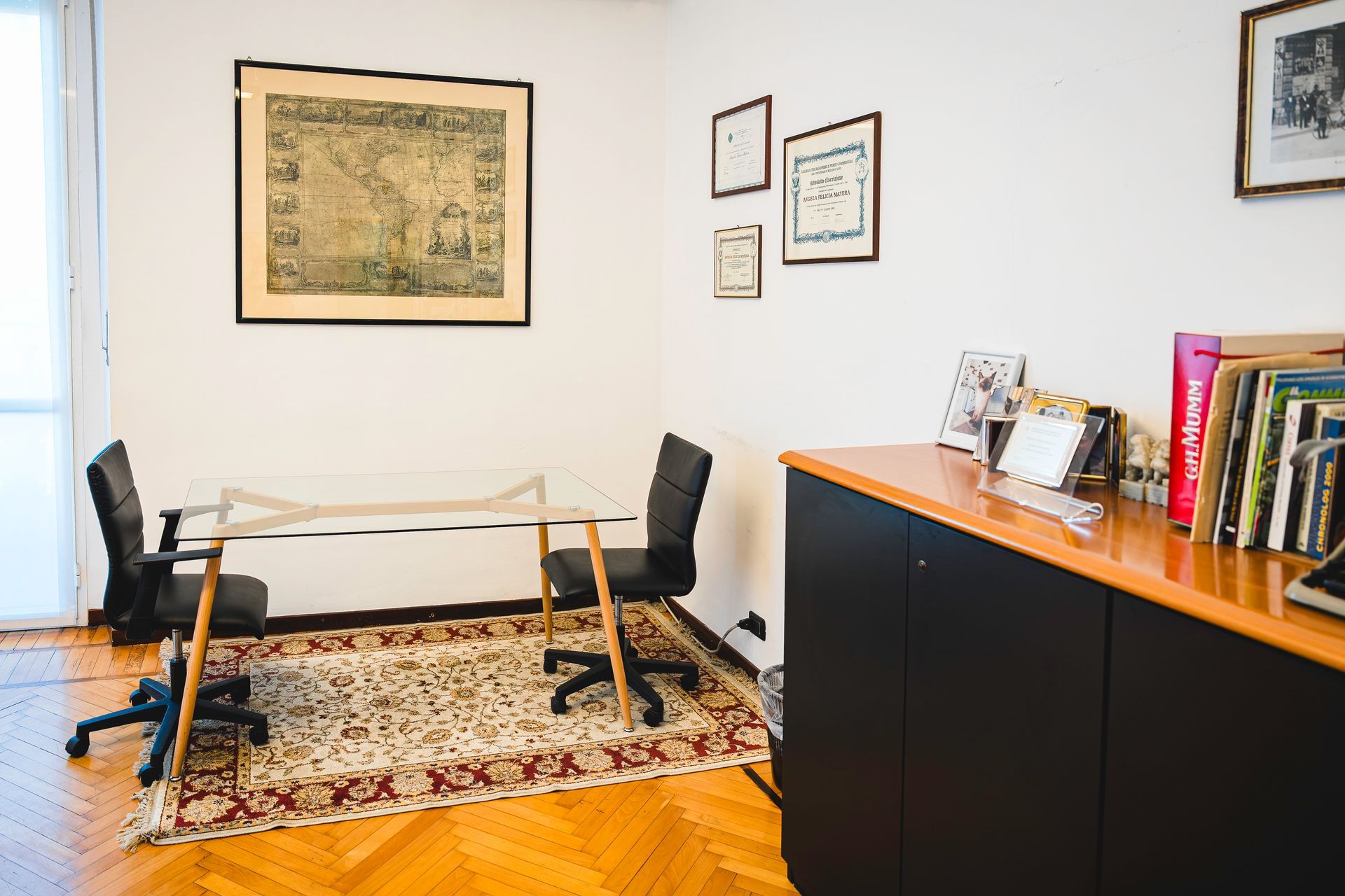 Due uomini in giacca e cravatta, uno seduto a una scrivania, l'altro in piedi, in un ufficio con documenti e una finestra.