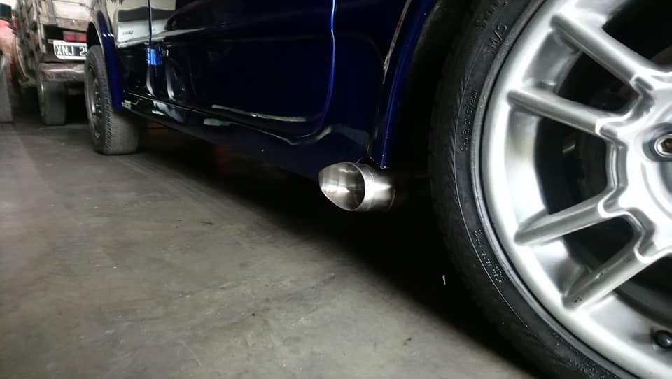 Un coche azul está aparcado en un garaje con un tubo de escape en el lateral.