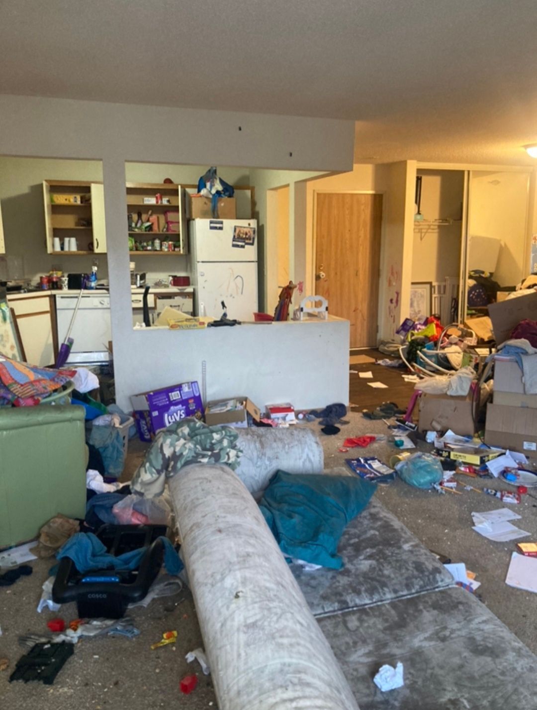 A living room in a messy house with a couch and a refrigerator.