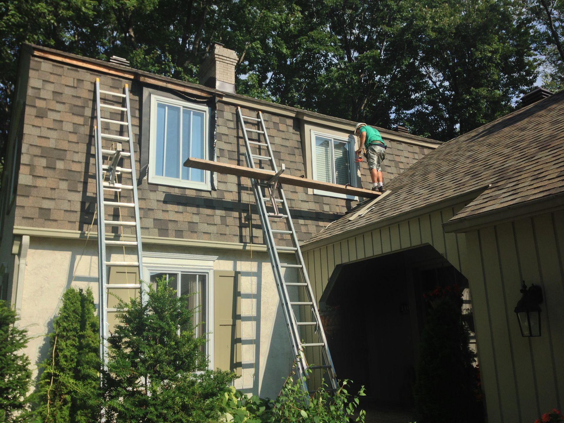 A man is standing on a ladder on the roof of a house.