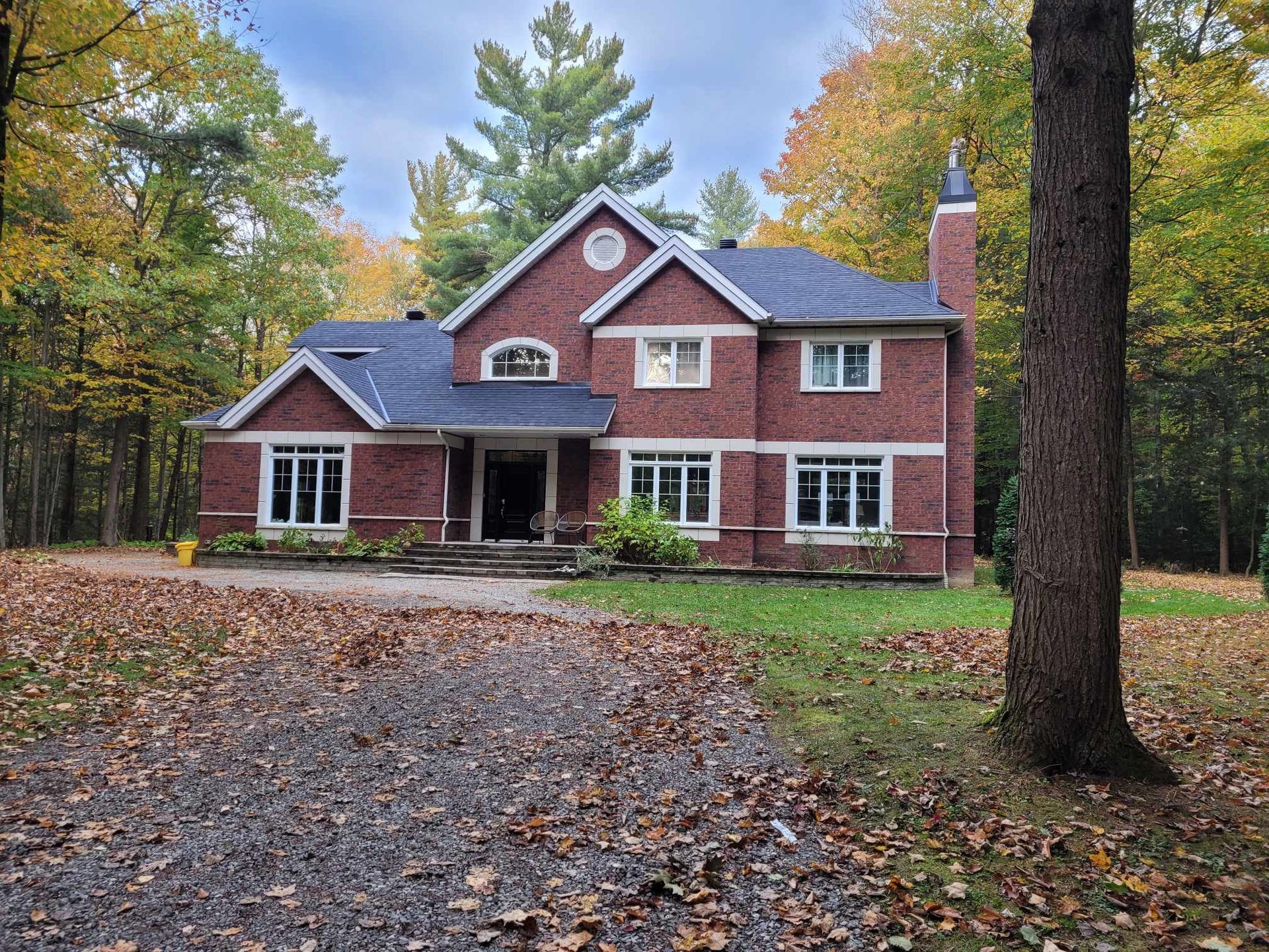 Une grande maison en briques rouges est entourée d'arbres et de feuilles.